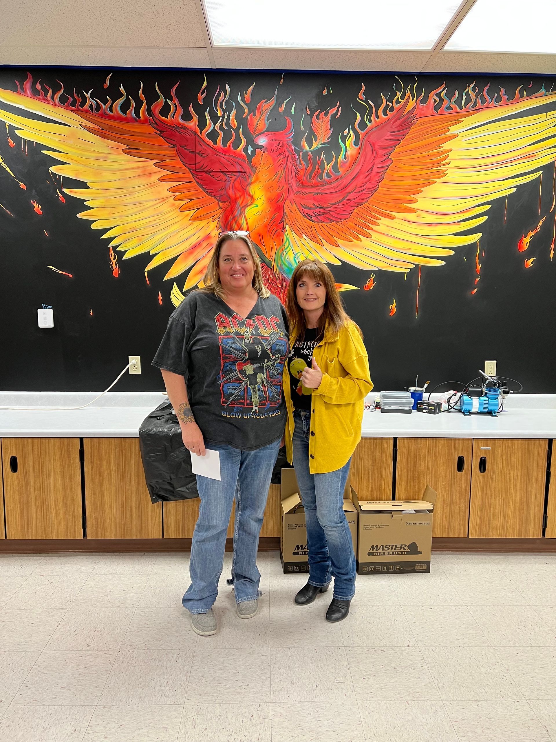 Two women are standing in front of a mural of a phoenix.