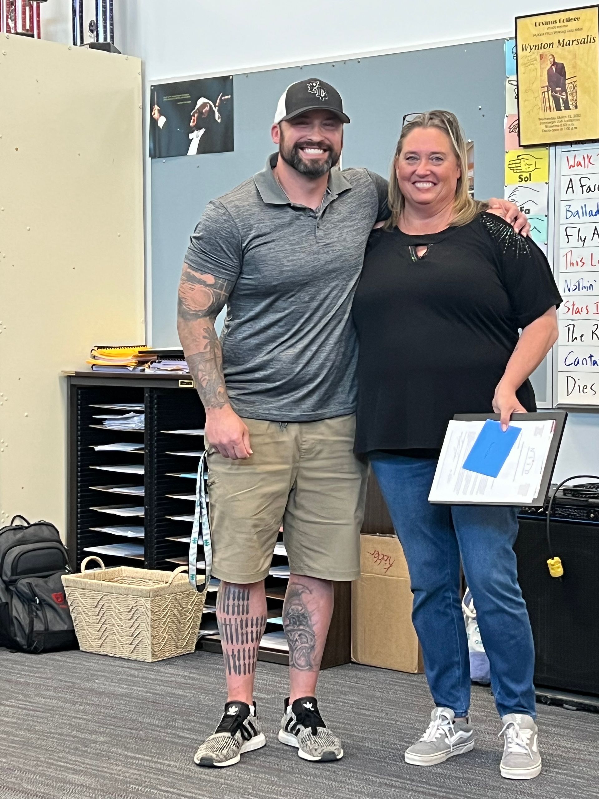 A man and a woman are posing for a picture in a classroom.