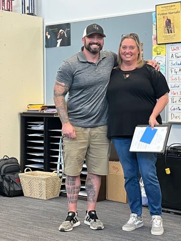 A man and a woman are posing for a picture in a classroom.
