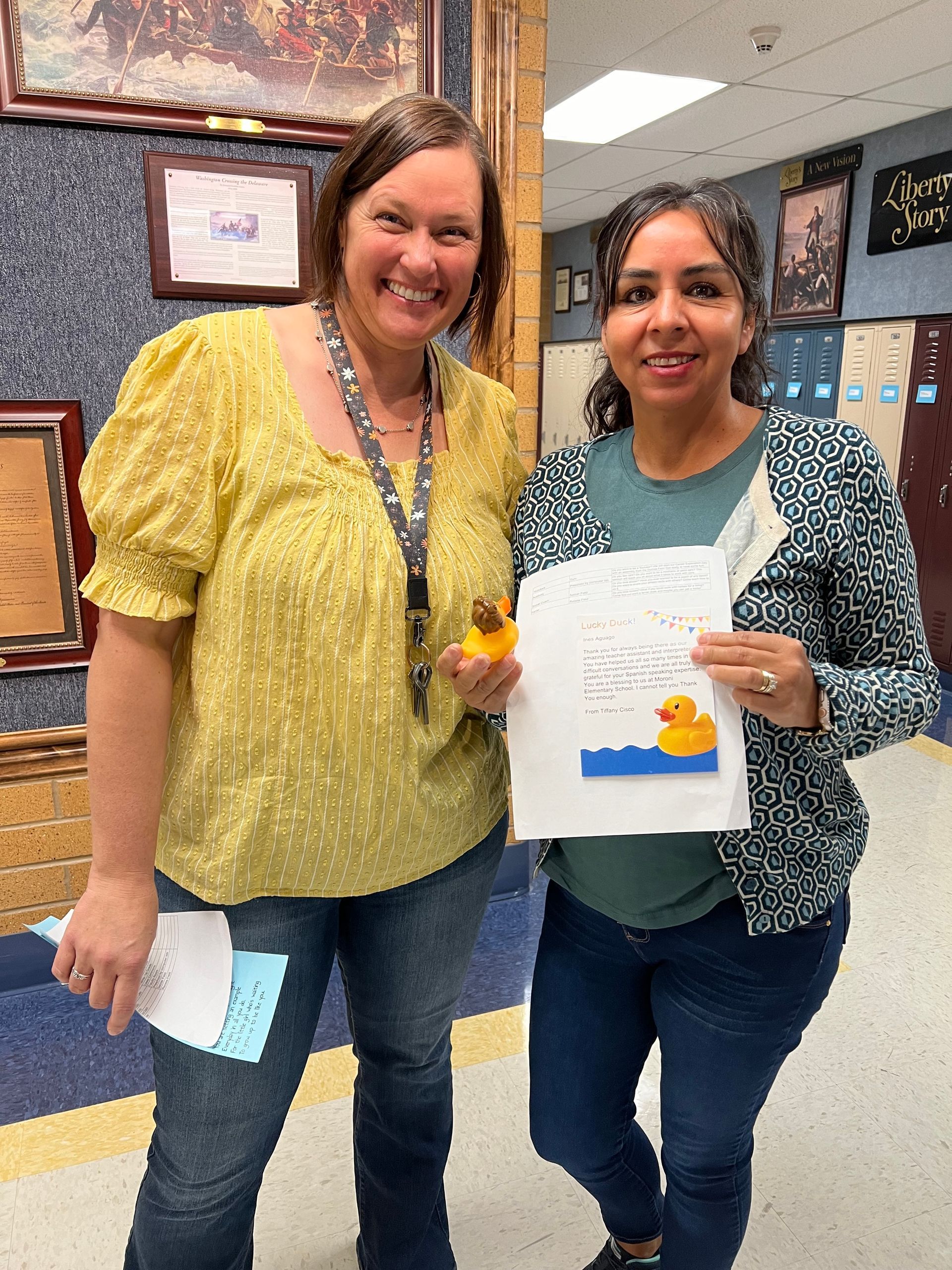 Two women are standing next to each other holding a rubber duck and a piece of paper.