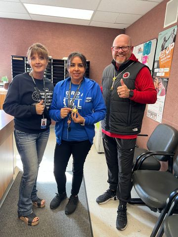 Three people indoors, smiling and holding keys, giving thumbs up.