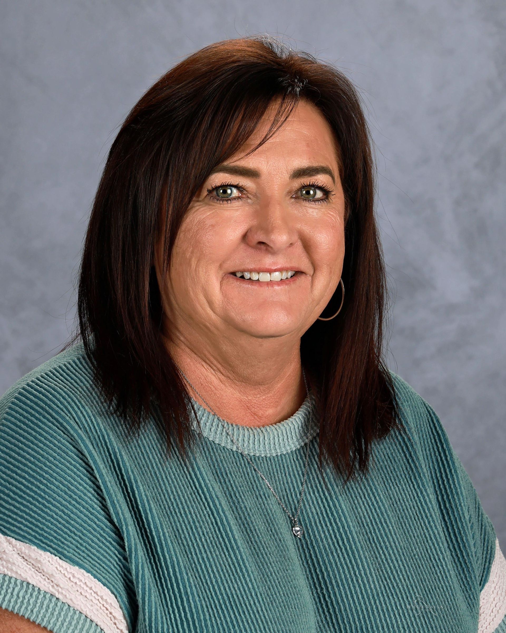 Woman with brown hair wearing a teal top smiles at the camera.