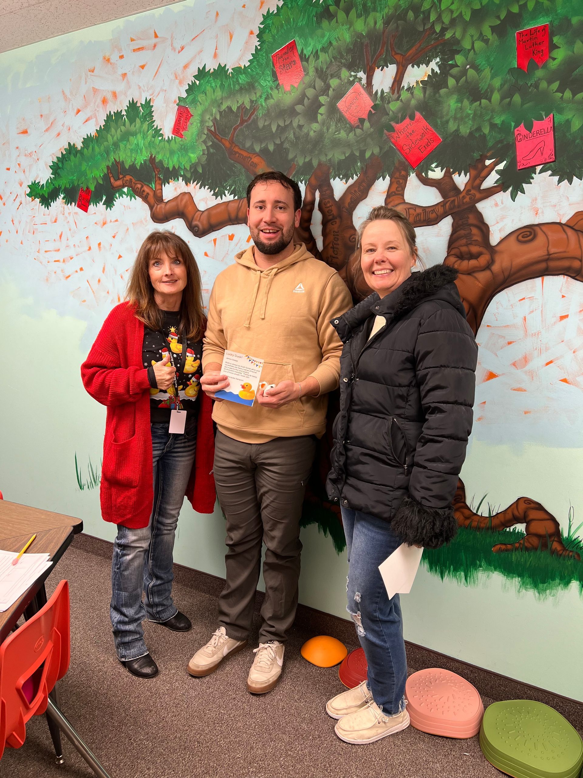 A man and two women are standing in front of a mural of an apple tree.