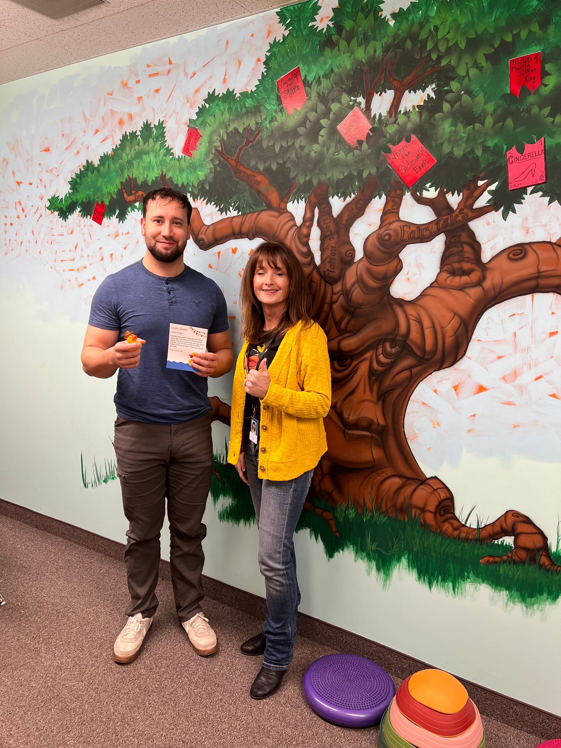 A man and a woman are standing in front of a painting of a tree.