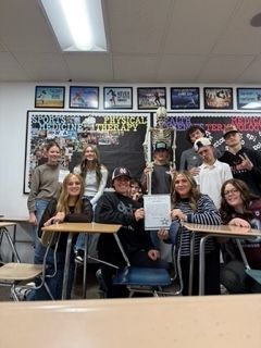 Group of students posing with a skeleton in a classroom.