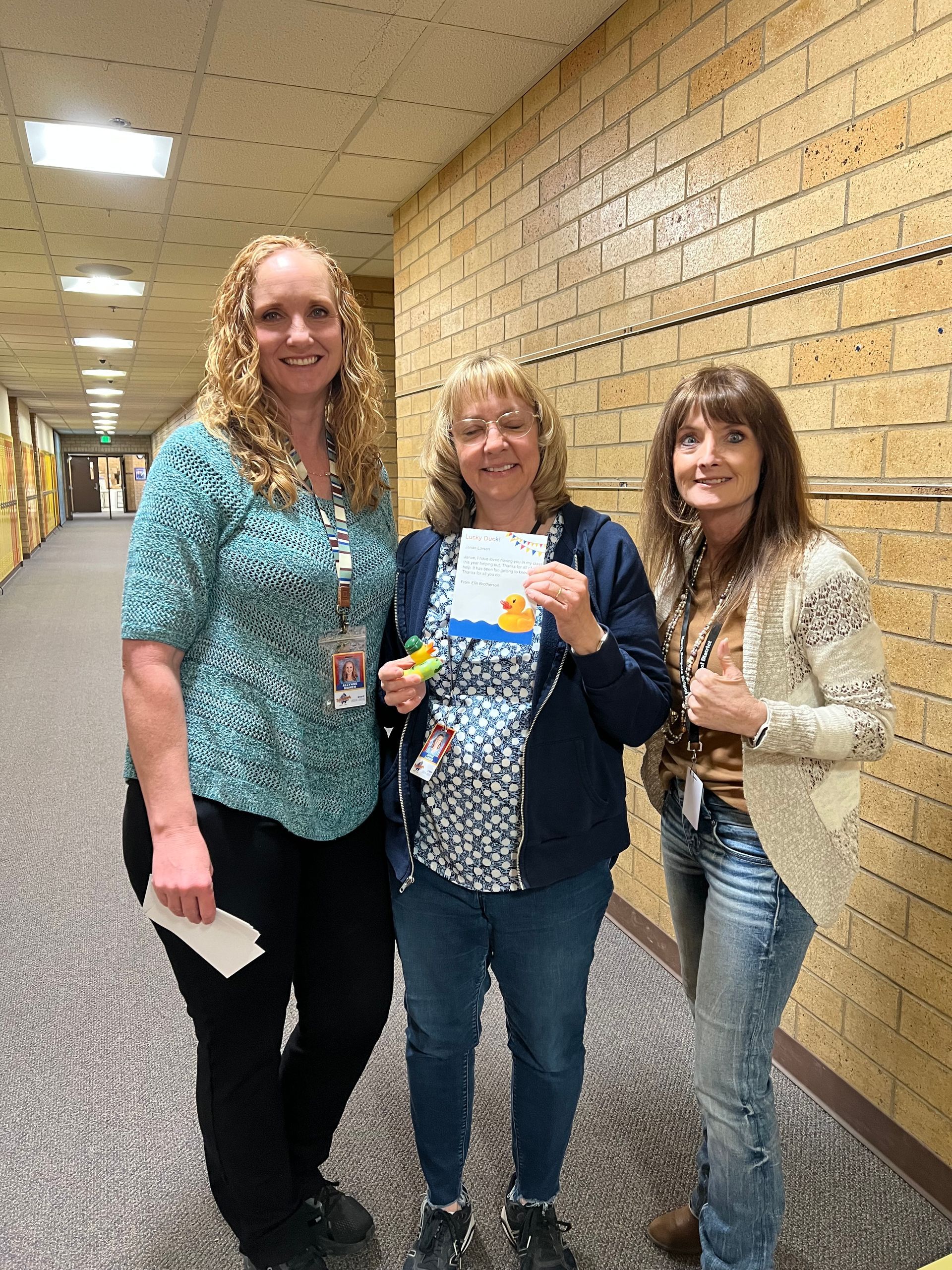 Three women are standing next to each other in a hallway.