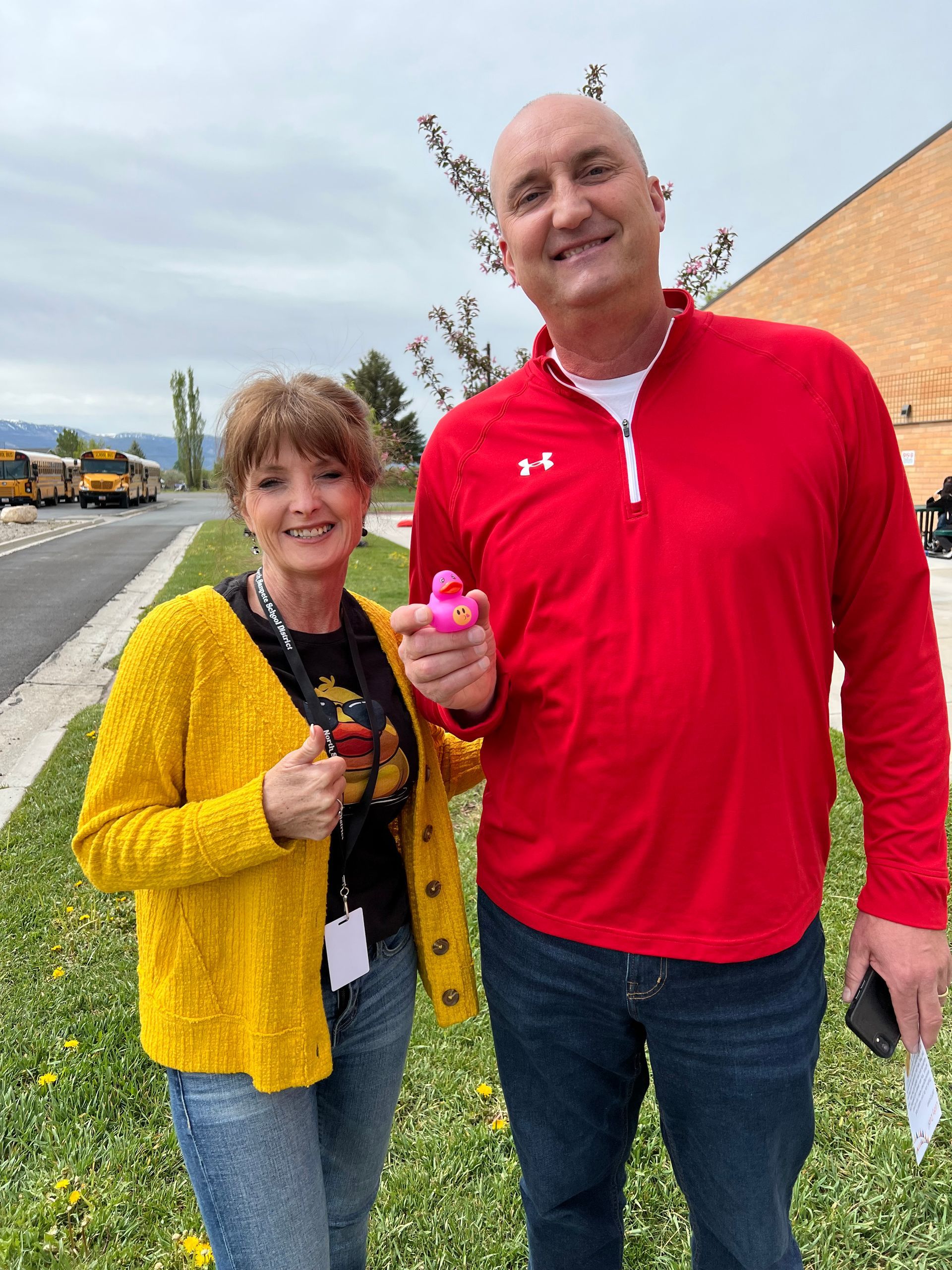 A man in a red shirt is standing next to a woman in a yellow sweater holding a pink rubber duck.