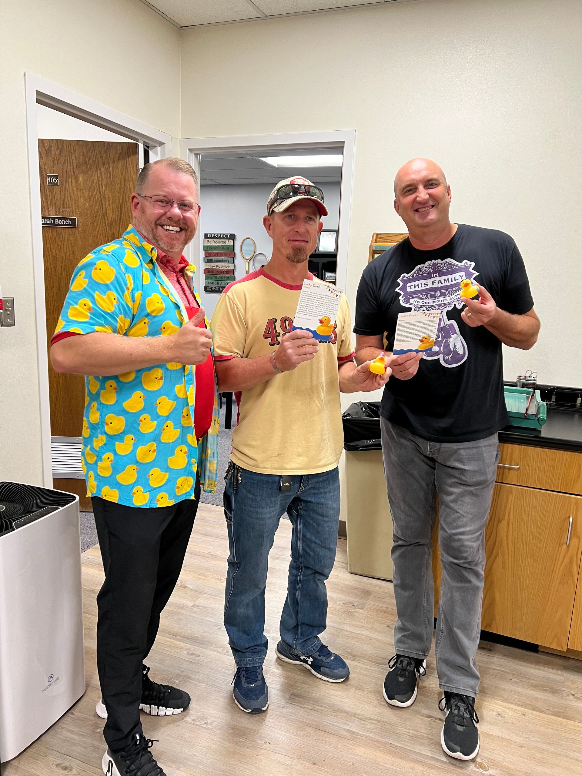 Three men are standing next to each other in a room holding plates of food.