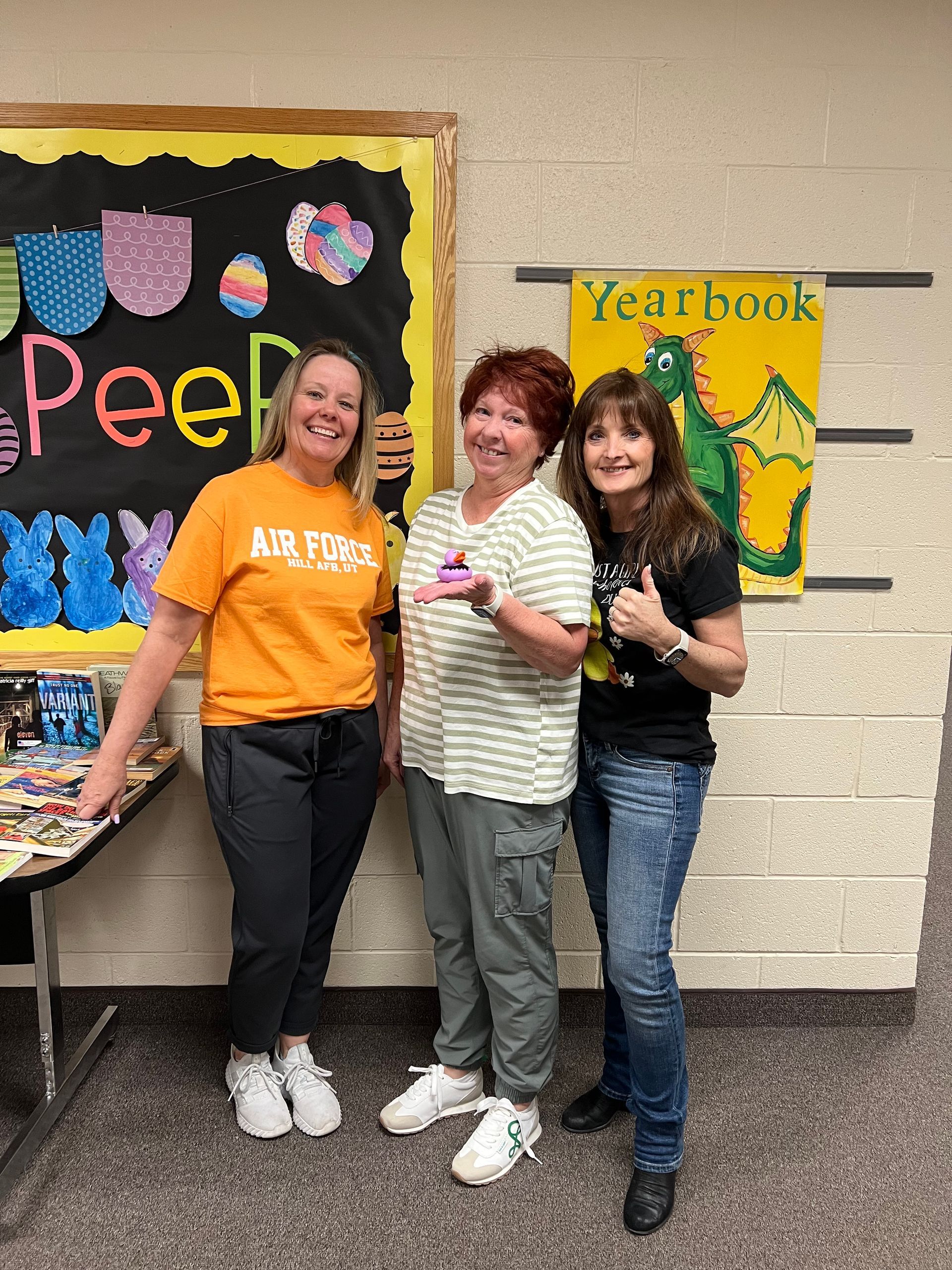 Three women are posing for a picture in front of a yearbook board.