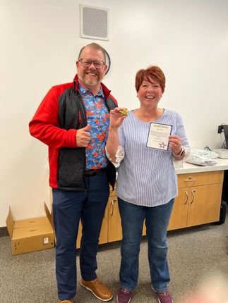 Two people smiling and holding drinks in a bright room beside stacked boxes and a cabinet
