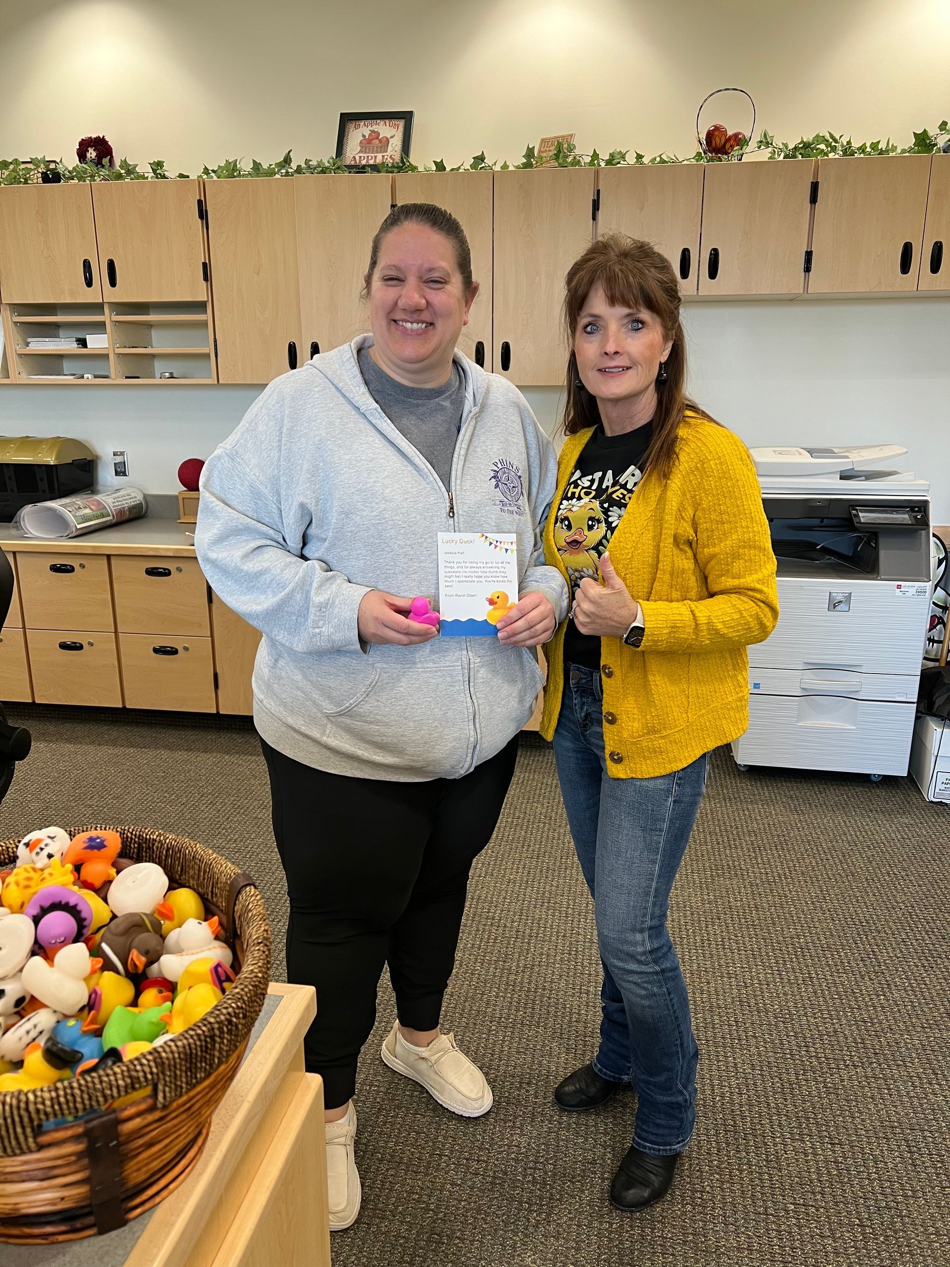 Two women are standing next to each other in a room holding a card.