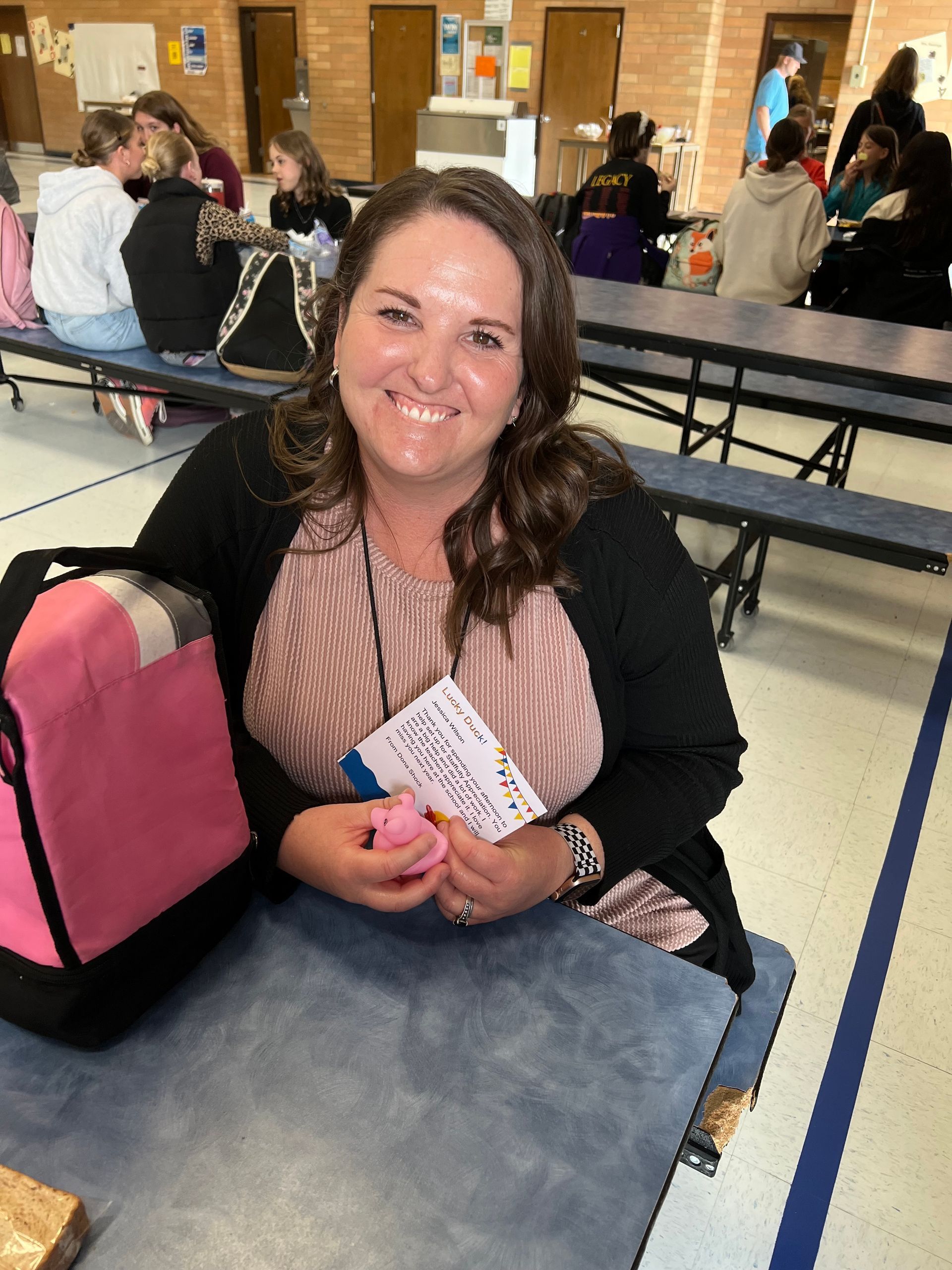 A woman is sitting at a table in a cafeteria holding a pink bag.
