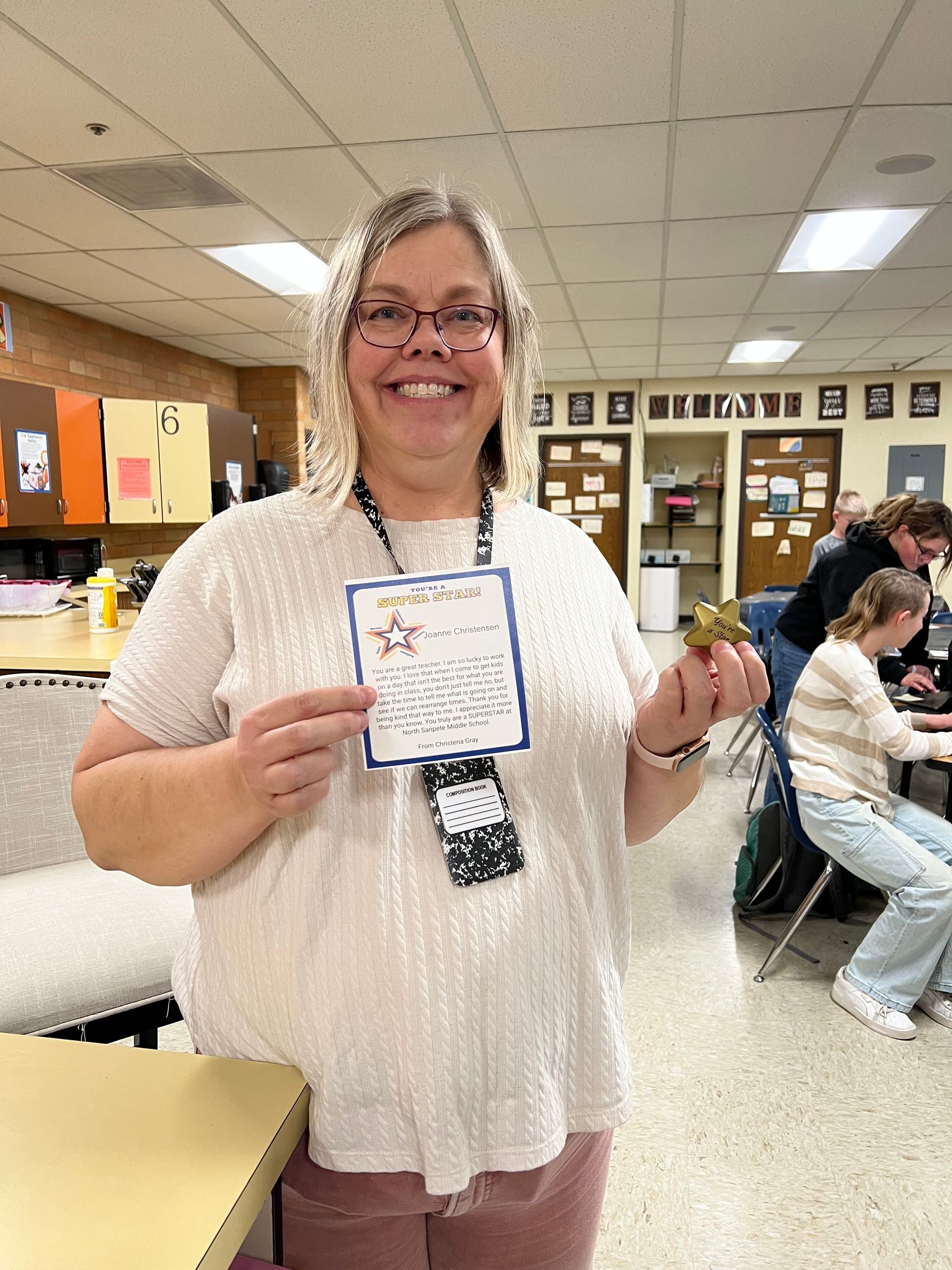 Woman holding a certificate and small object, smiling in a classroom setting.