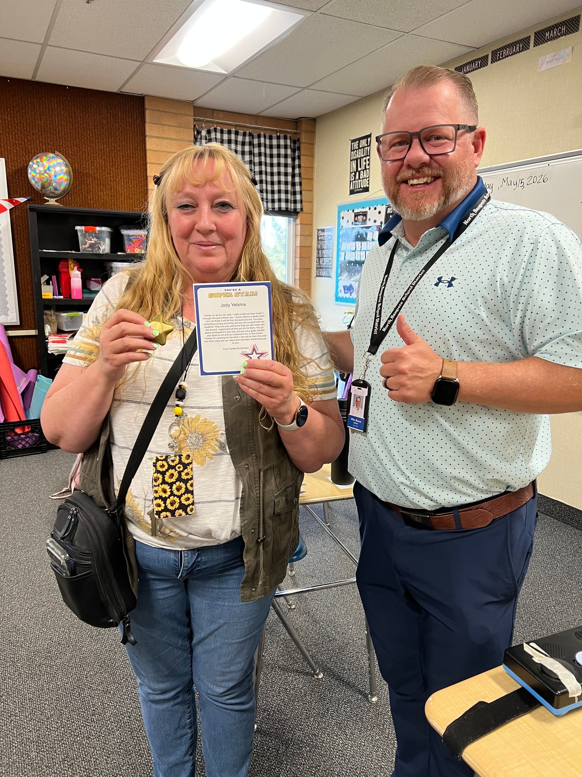 Two people smiling indoors, holding a certificate and a small fish at a counter.