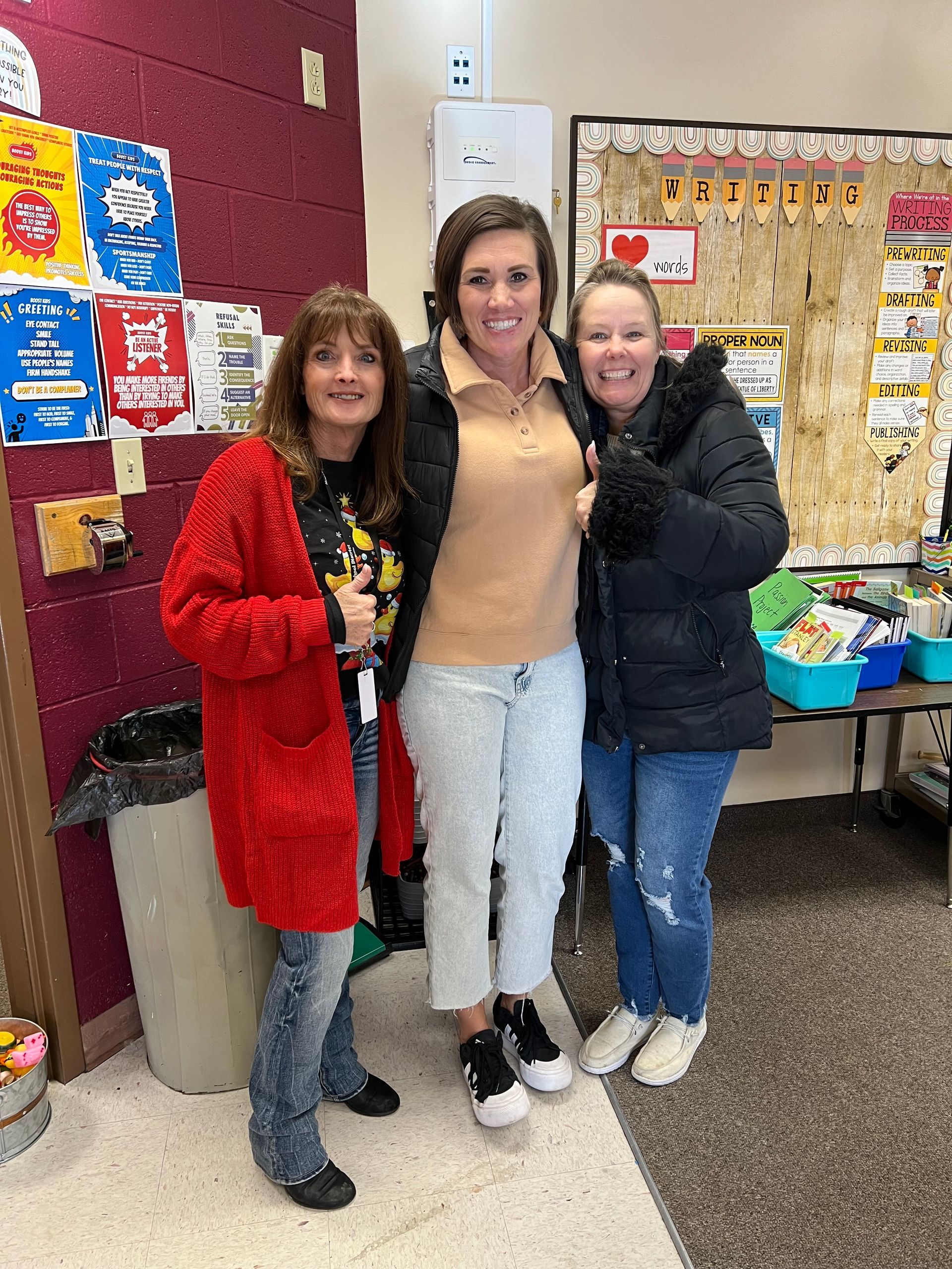 Three women are posing for a picture in a classroom.