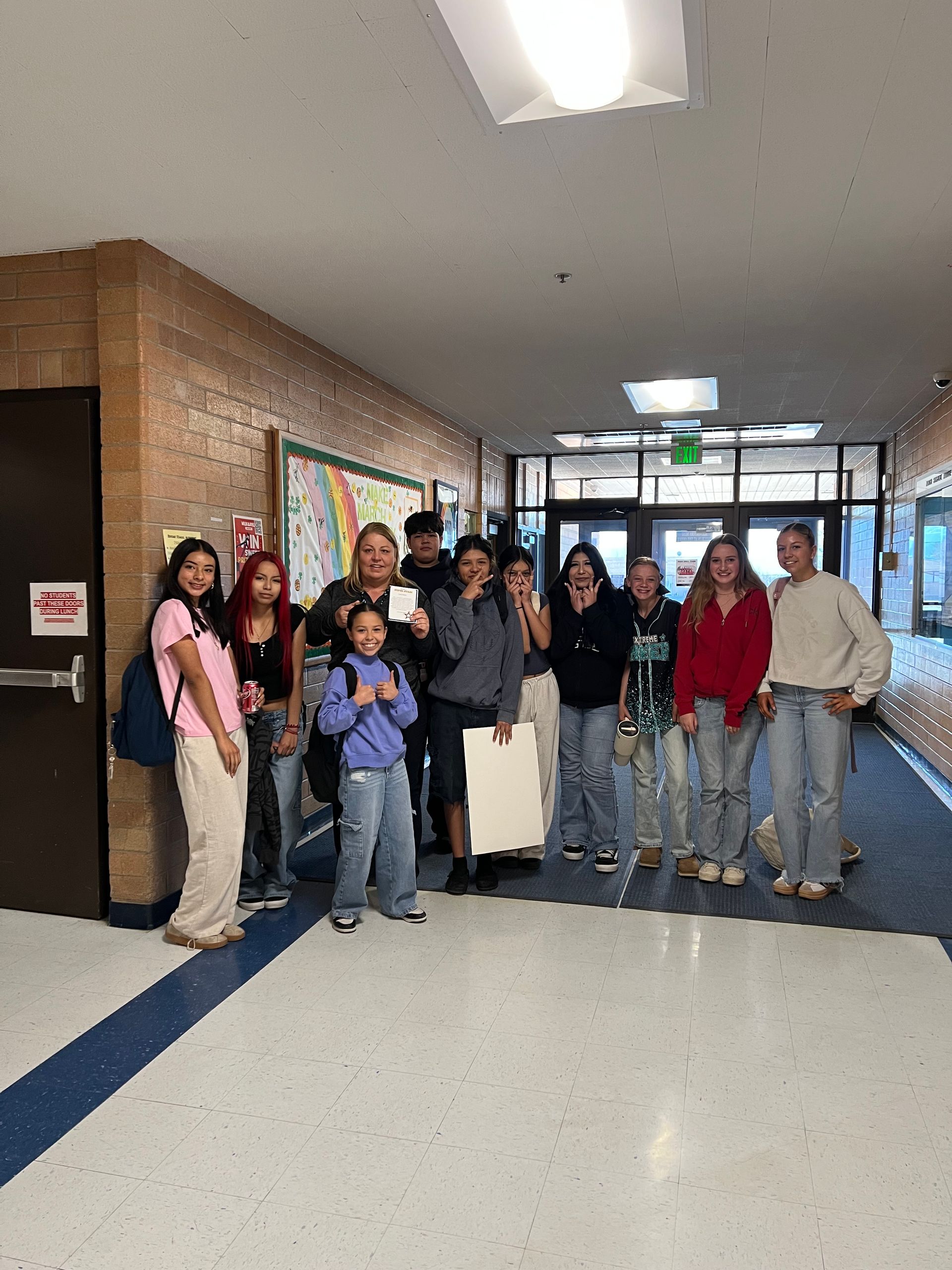 A group of people standing in a school hallway near an entrance, posing for a group photo.