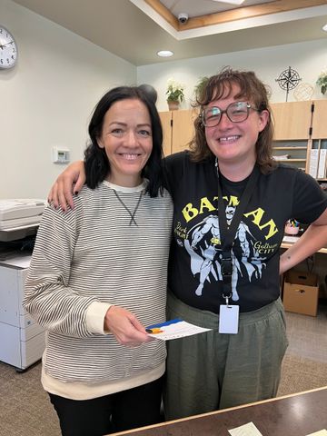 Two women are standing next to each other in a room and smiling.