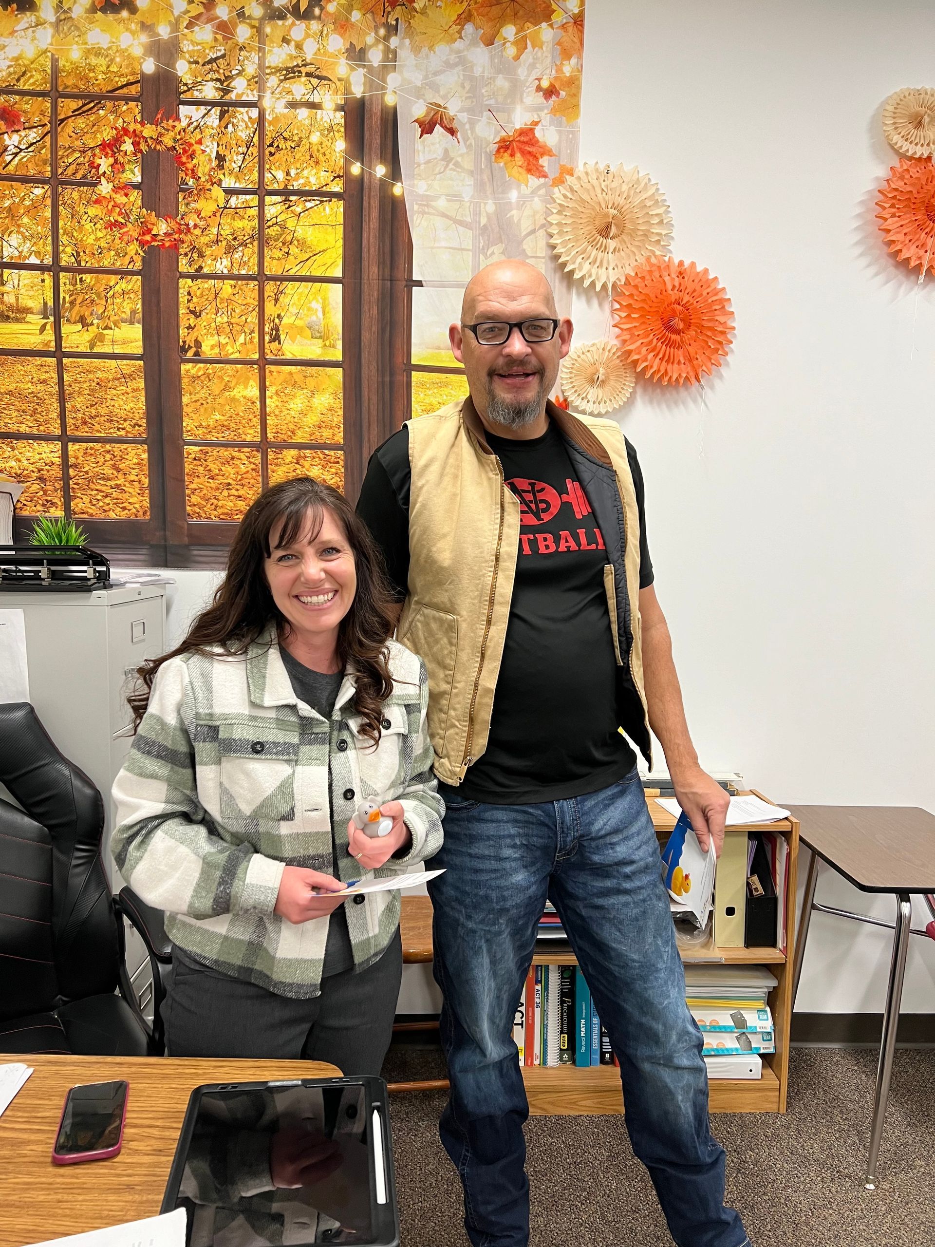 A man and a woman are standing next to each other in a classroom.