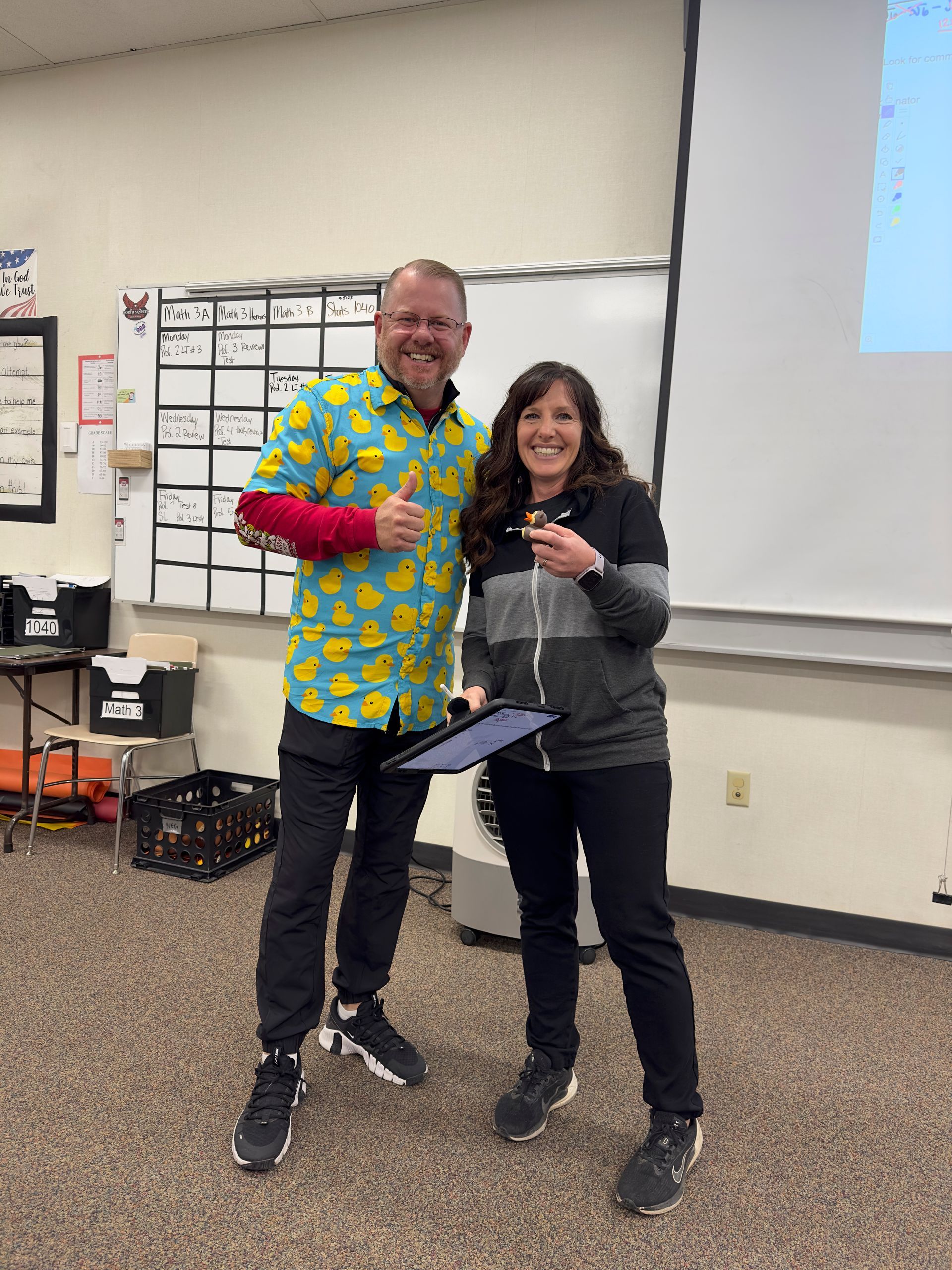 A man and a woman are standing next to each other in a classroom.