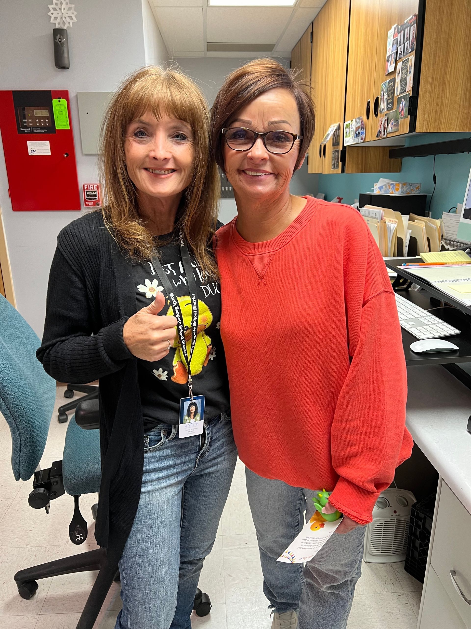 Two women are posing for a picture in an office.