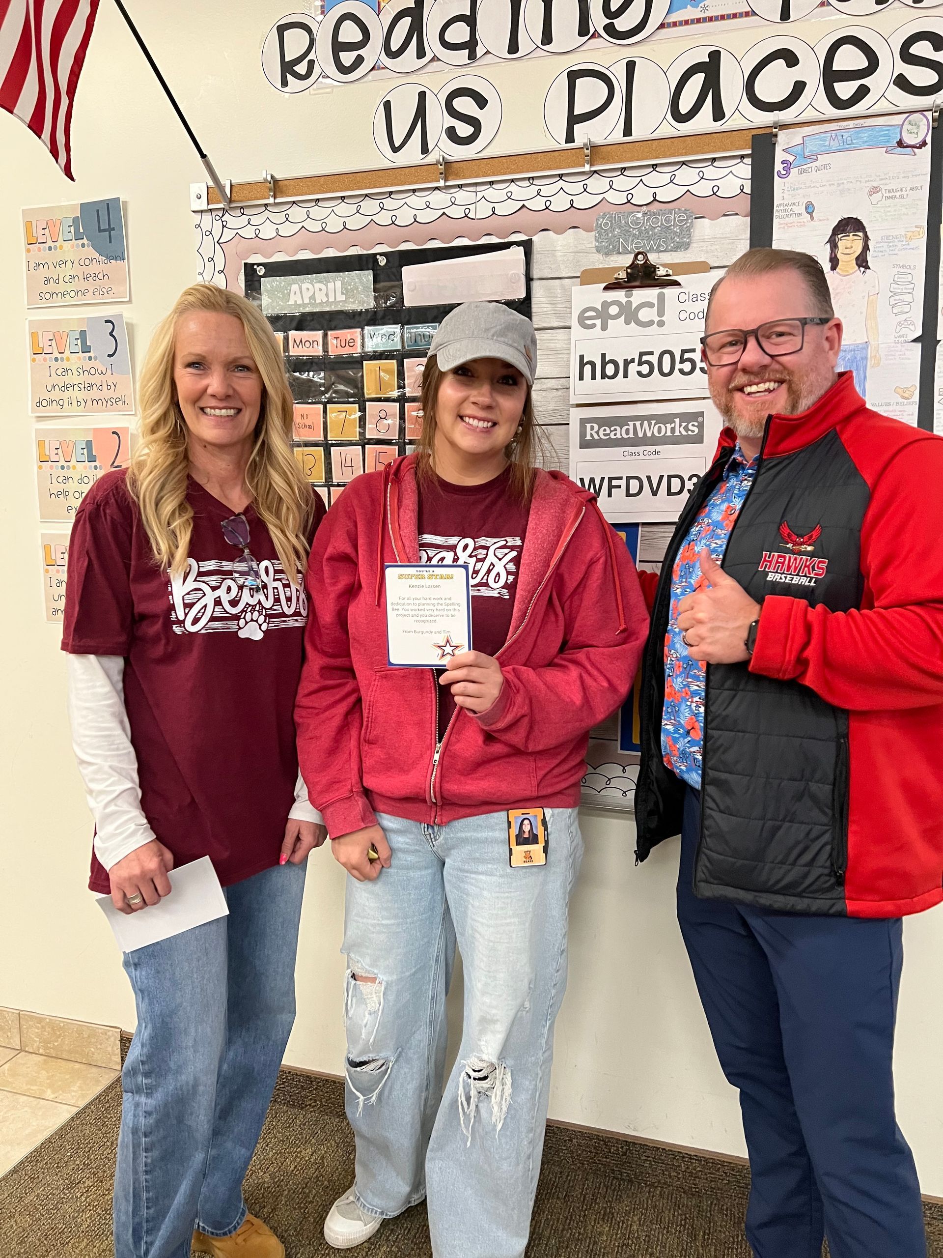 Three people in red sweatshirts pose indoors, with one holding a small sign.