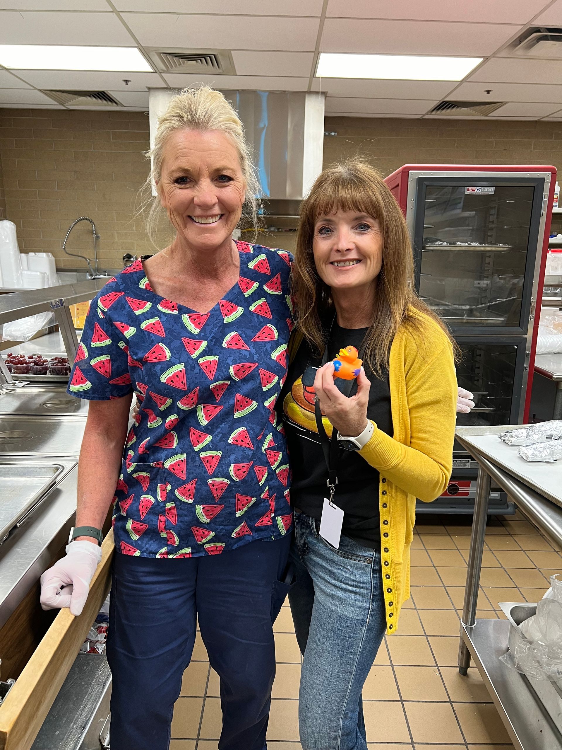 Two women are standing next to each other in a kitchen holding an orange.