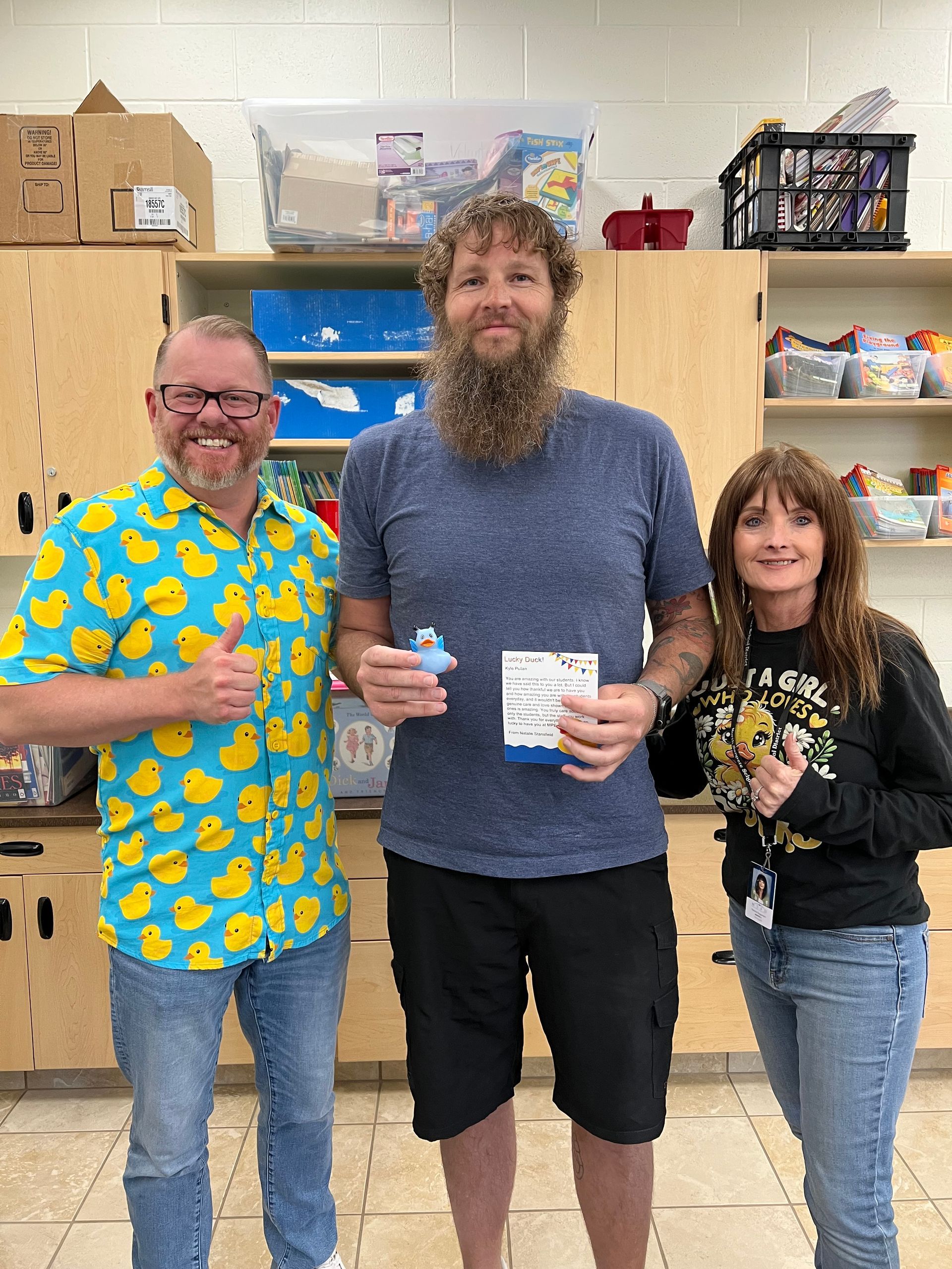 A man with a beard is standing next to two other people in a kitchen.