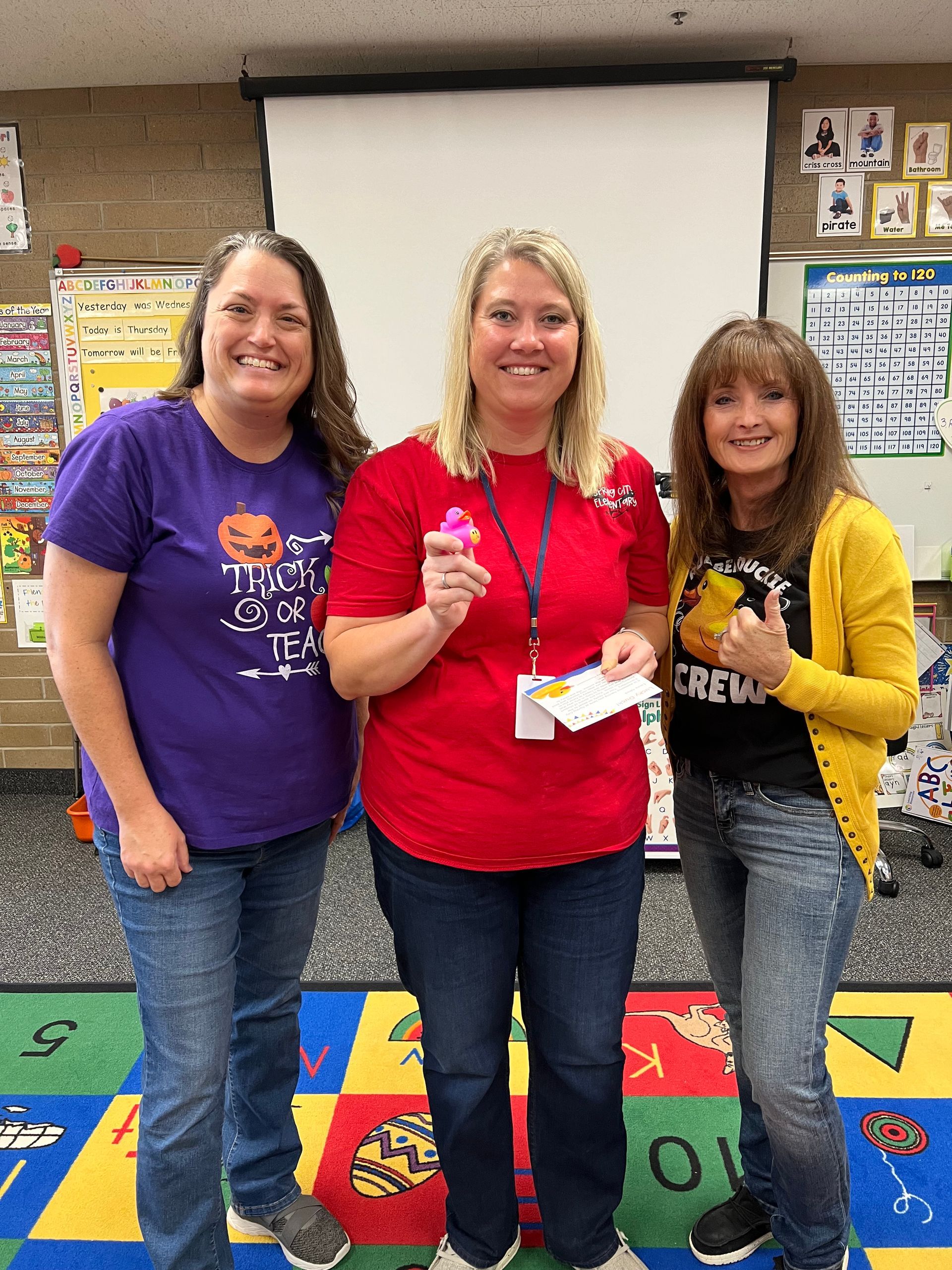 Three women are standing next to each other in a classroom.