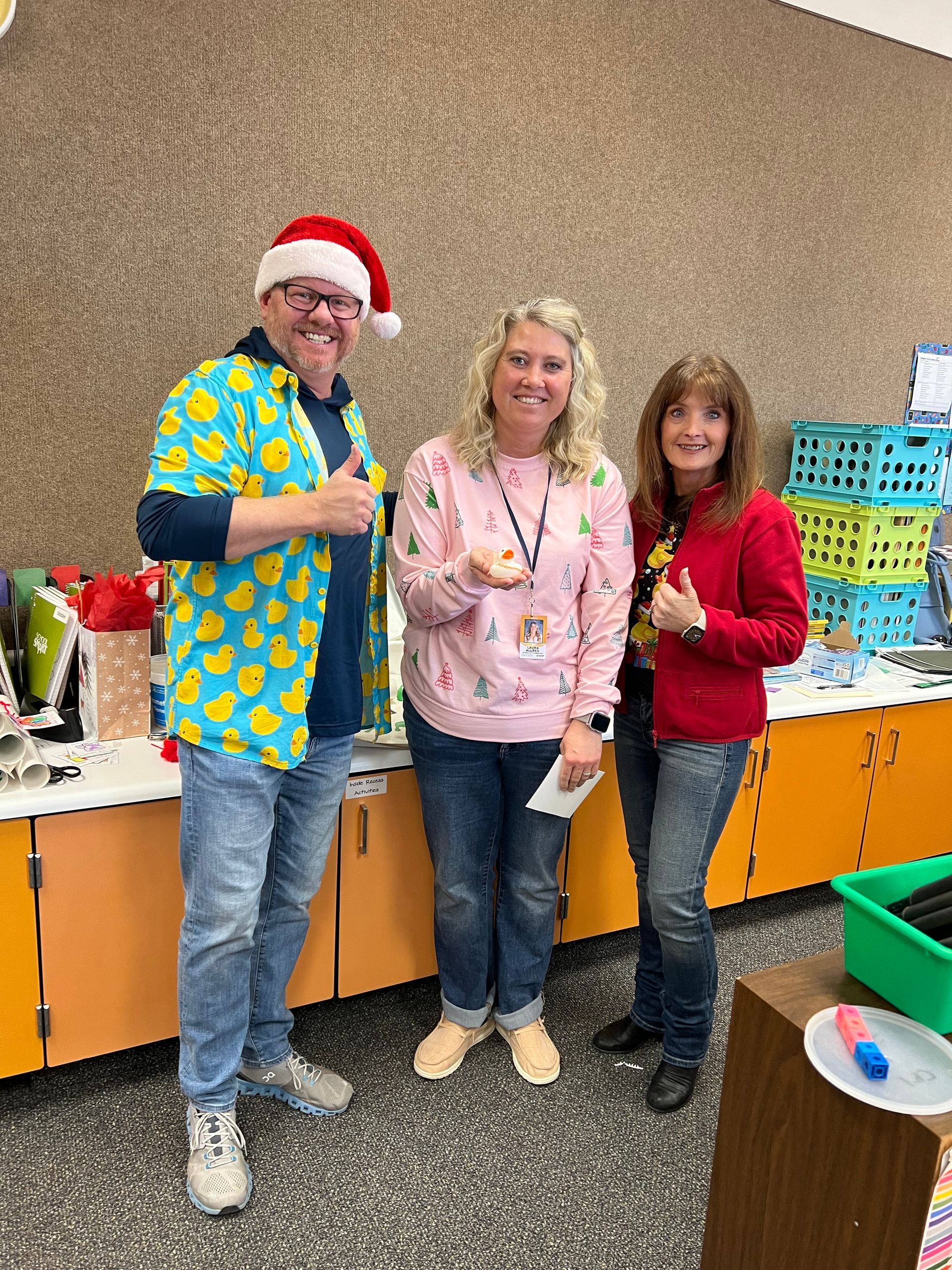 A man wearing a santa hat is standing next to two women in a kitchen.