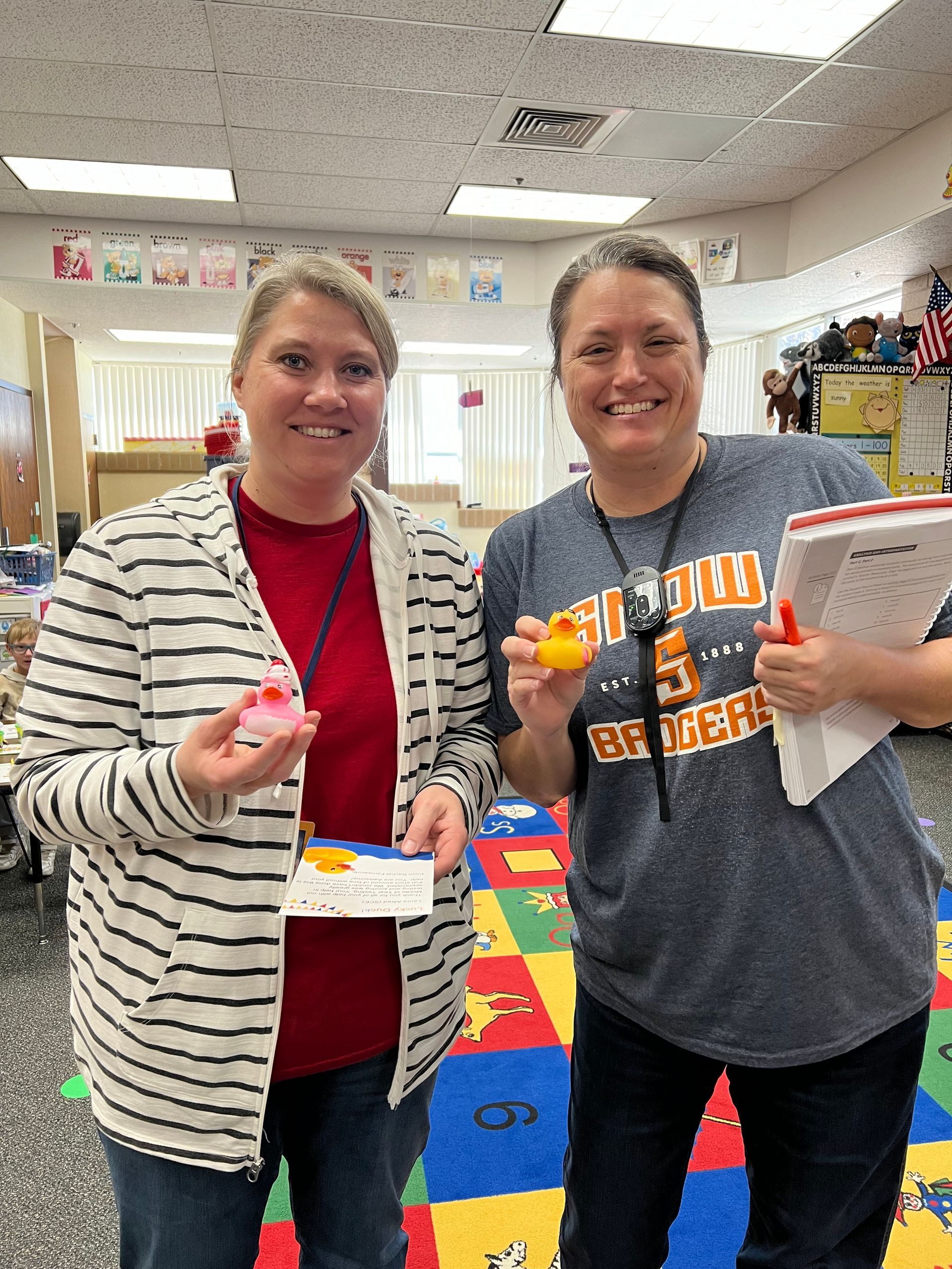 Two women are standing next to each other in a classroom holding toys.