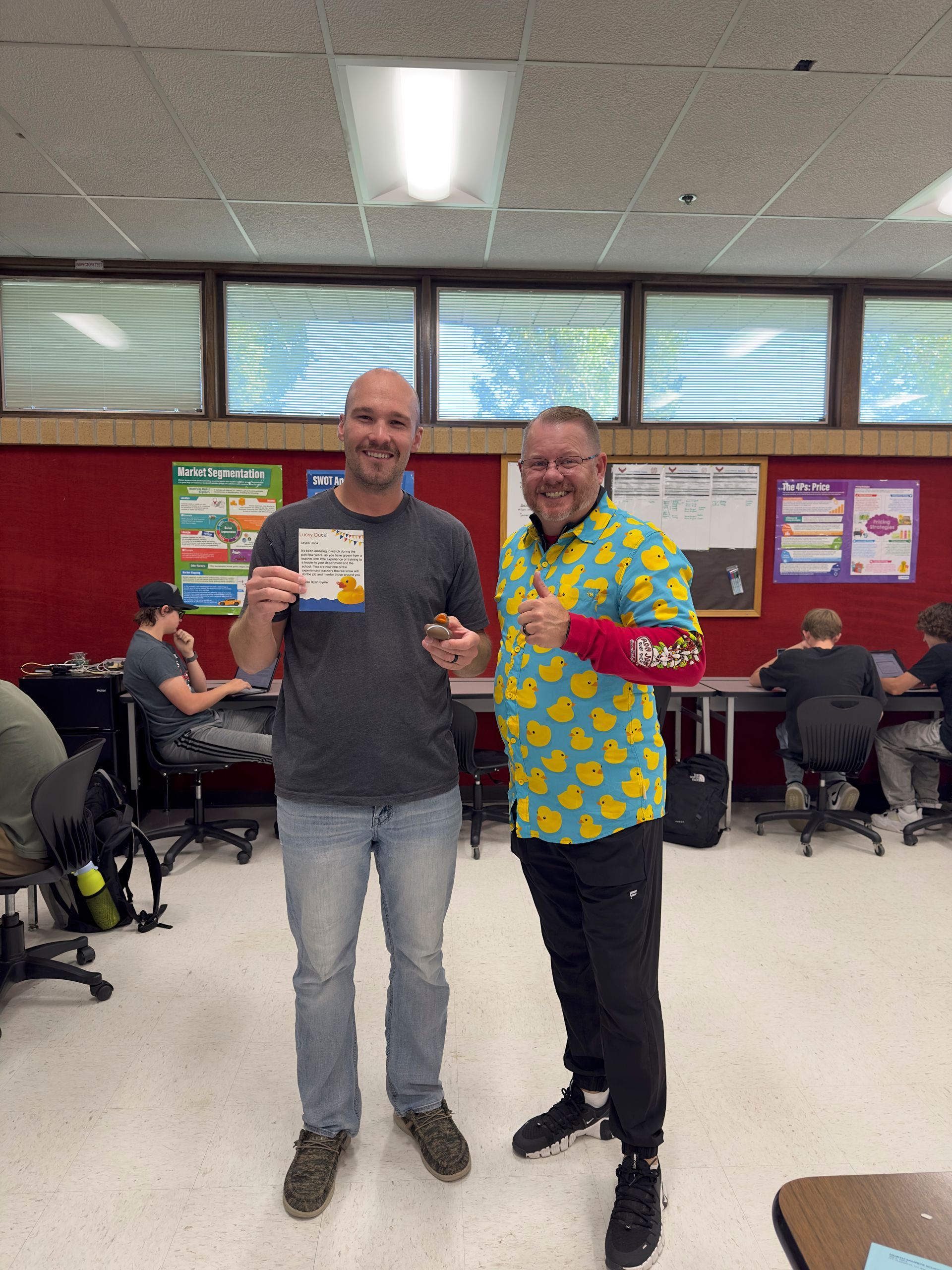 Two men are standing next to each other in a classroom holding a certificate.