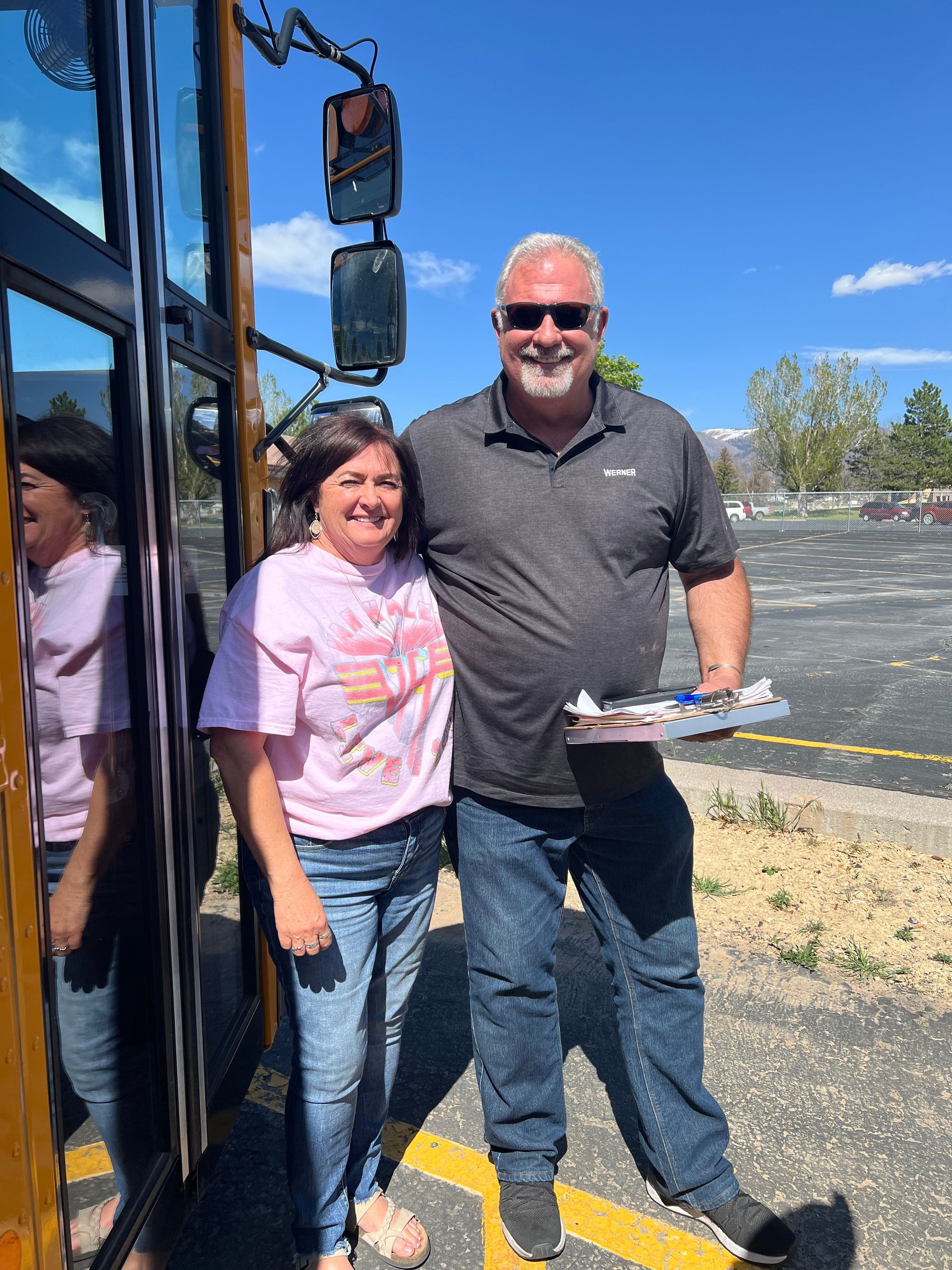 Two people standing beside a bus on a sunny day, one holding a plate of food.