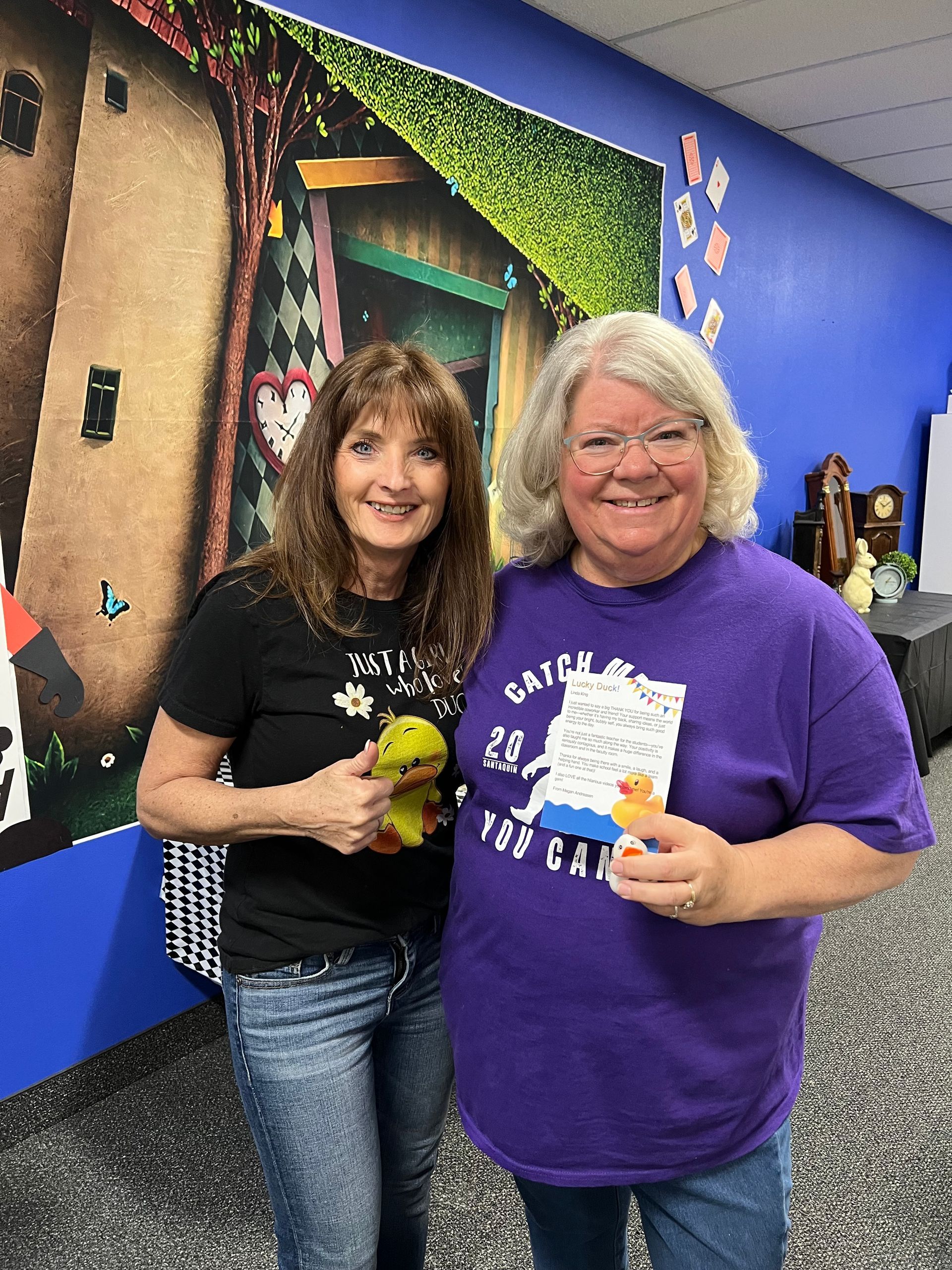 Two women are posing for a picture in a room . one of the women is wearing a purple shirt.