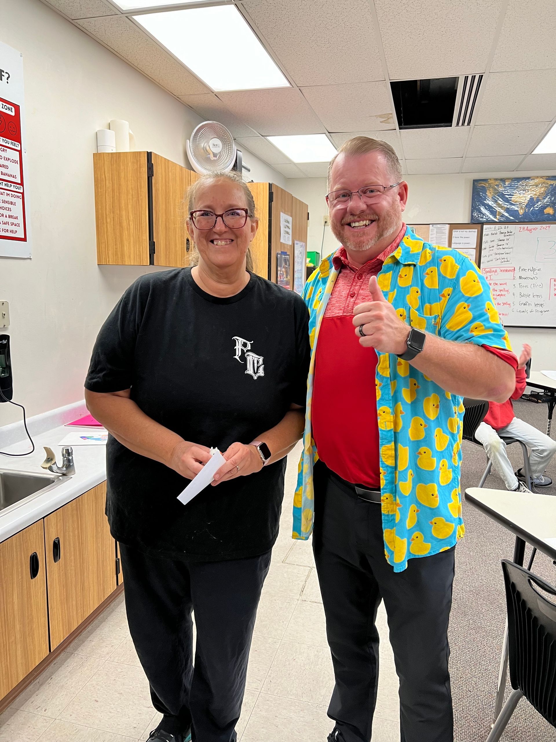 A man and a woman are standing next to each other in a classroom.