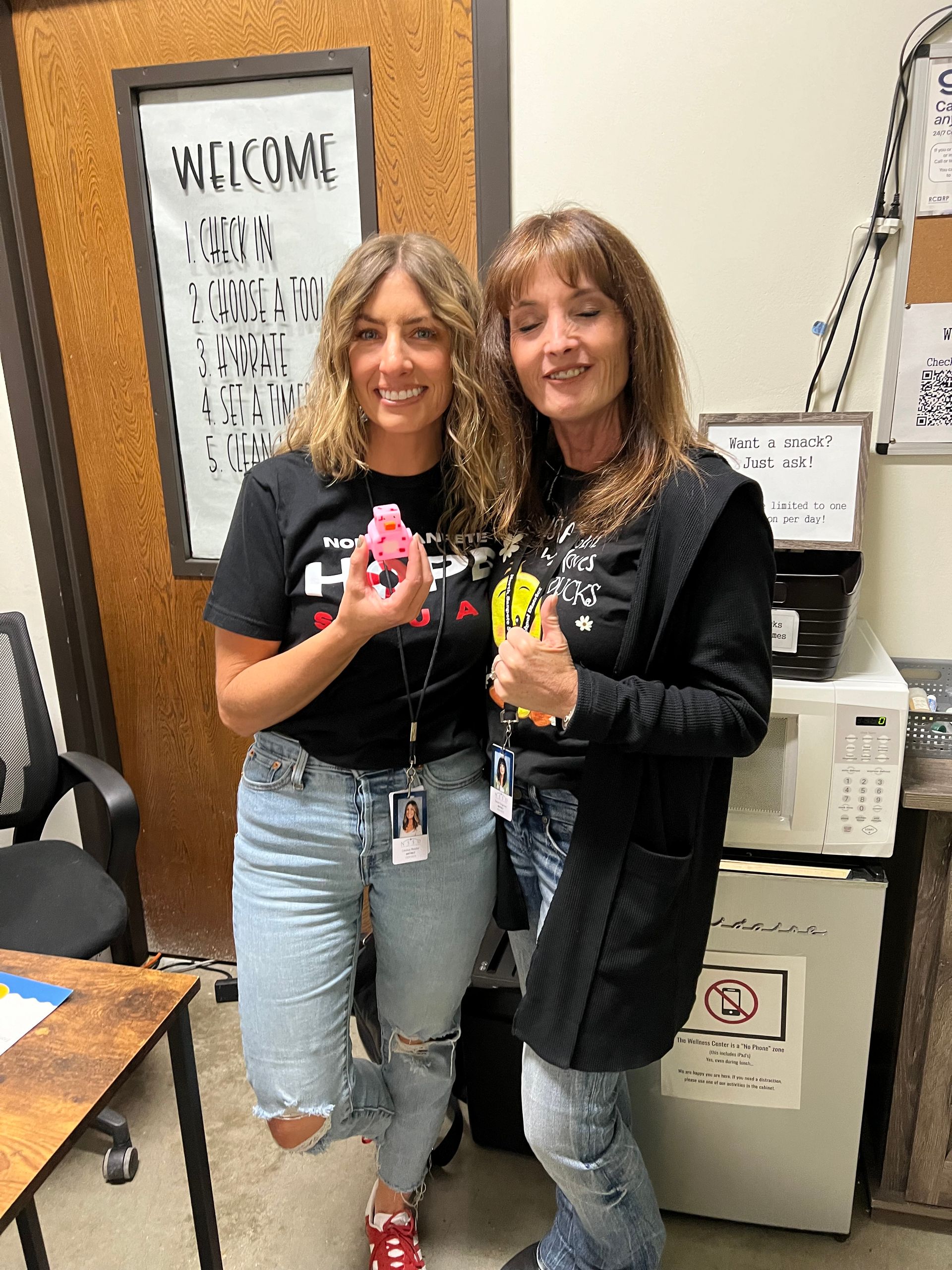 Two women are standing next to each other in a room and smiling.