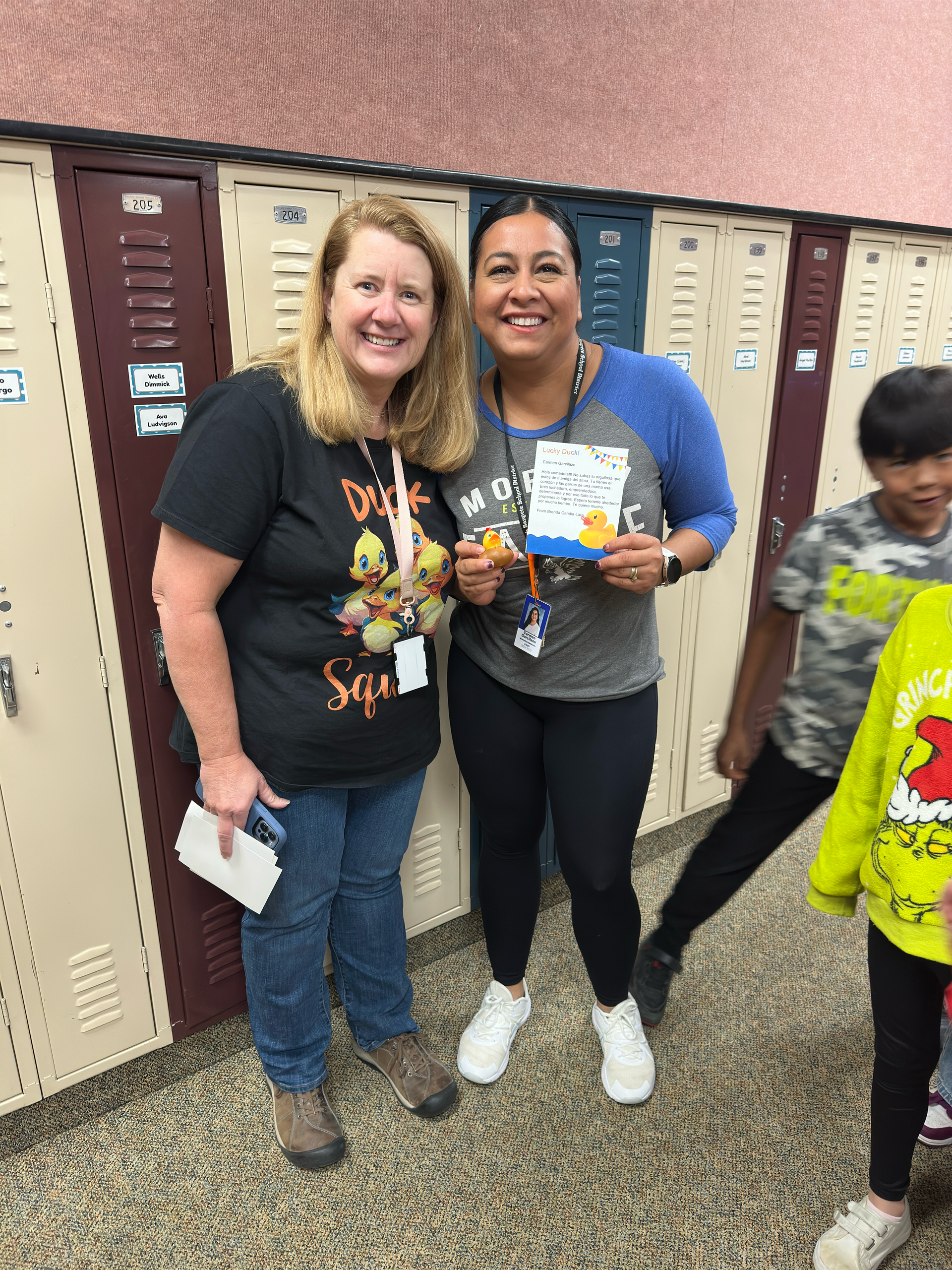 Two women are standing next to each other in front of lockers.