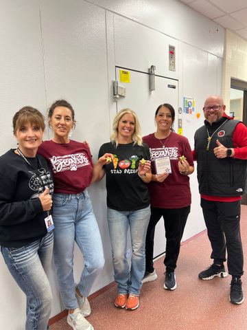 Five people pose in front of a walk-in freezer. They are holding food items, giving thumbs up and smiling.