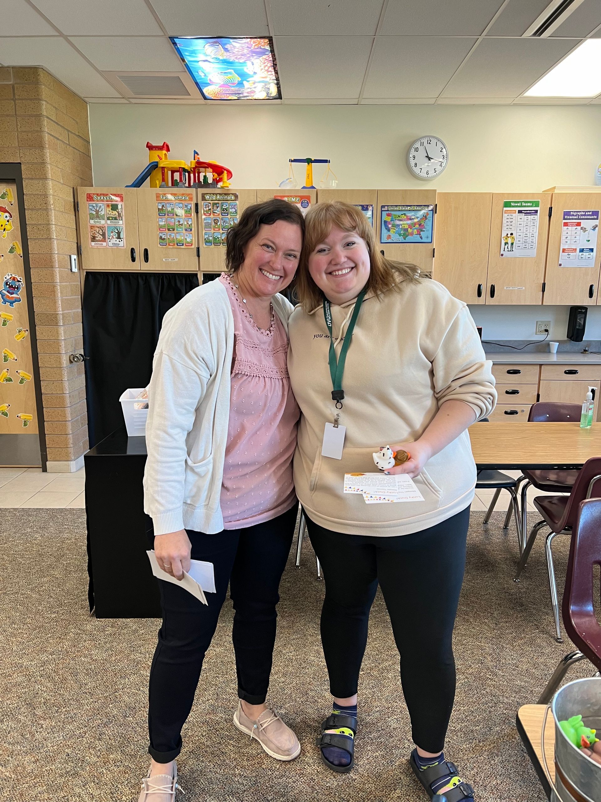 Two women are posing for a picture in a classroom.