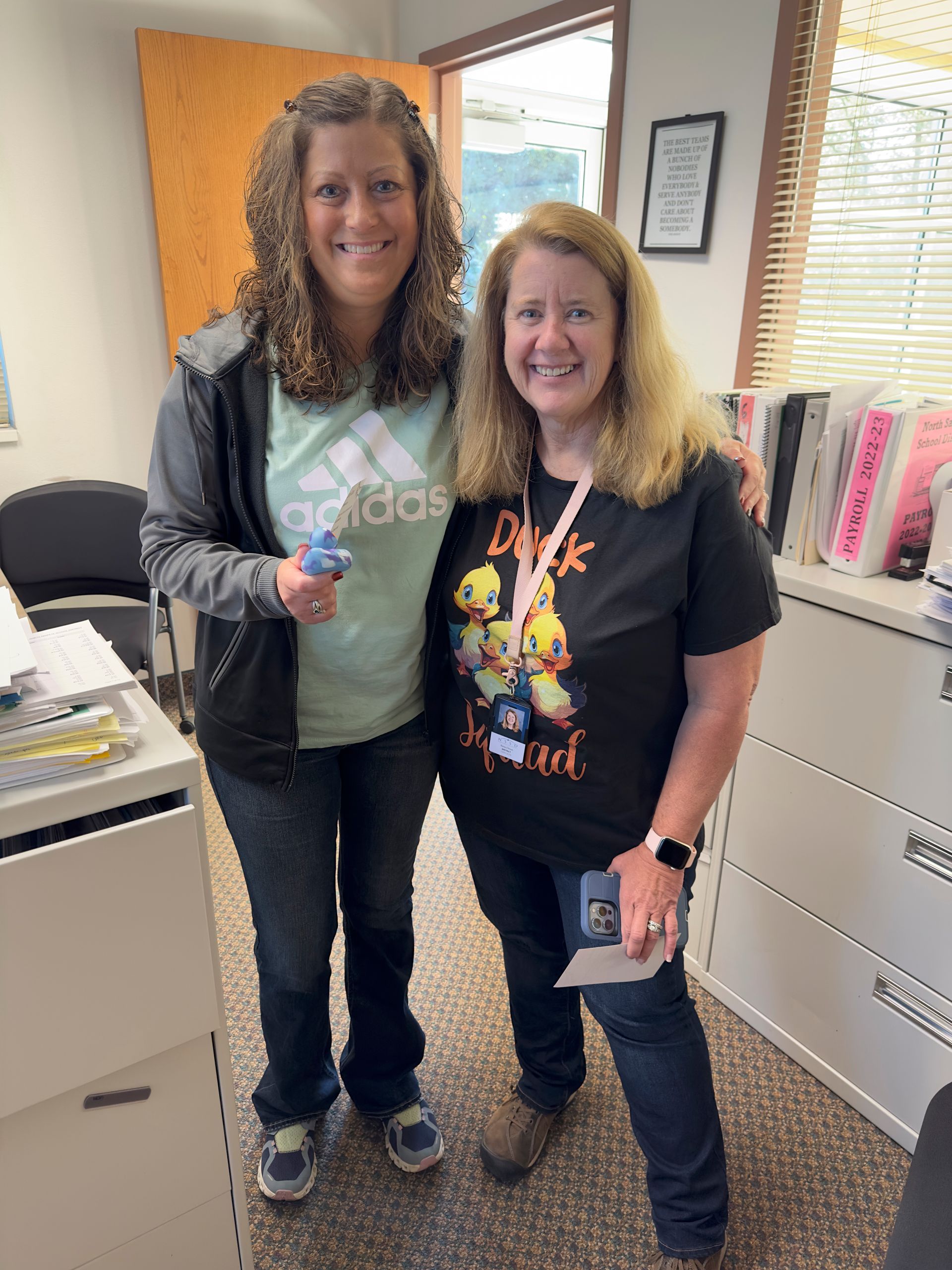 Two women are posing for a picture in a room . one of the women is wearing an adidas shirt.