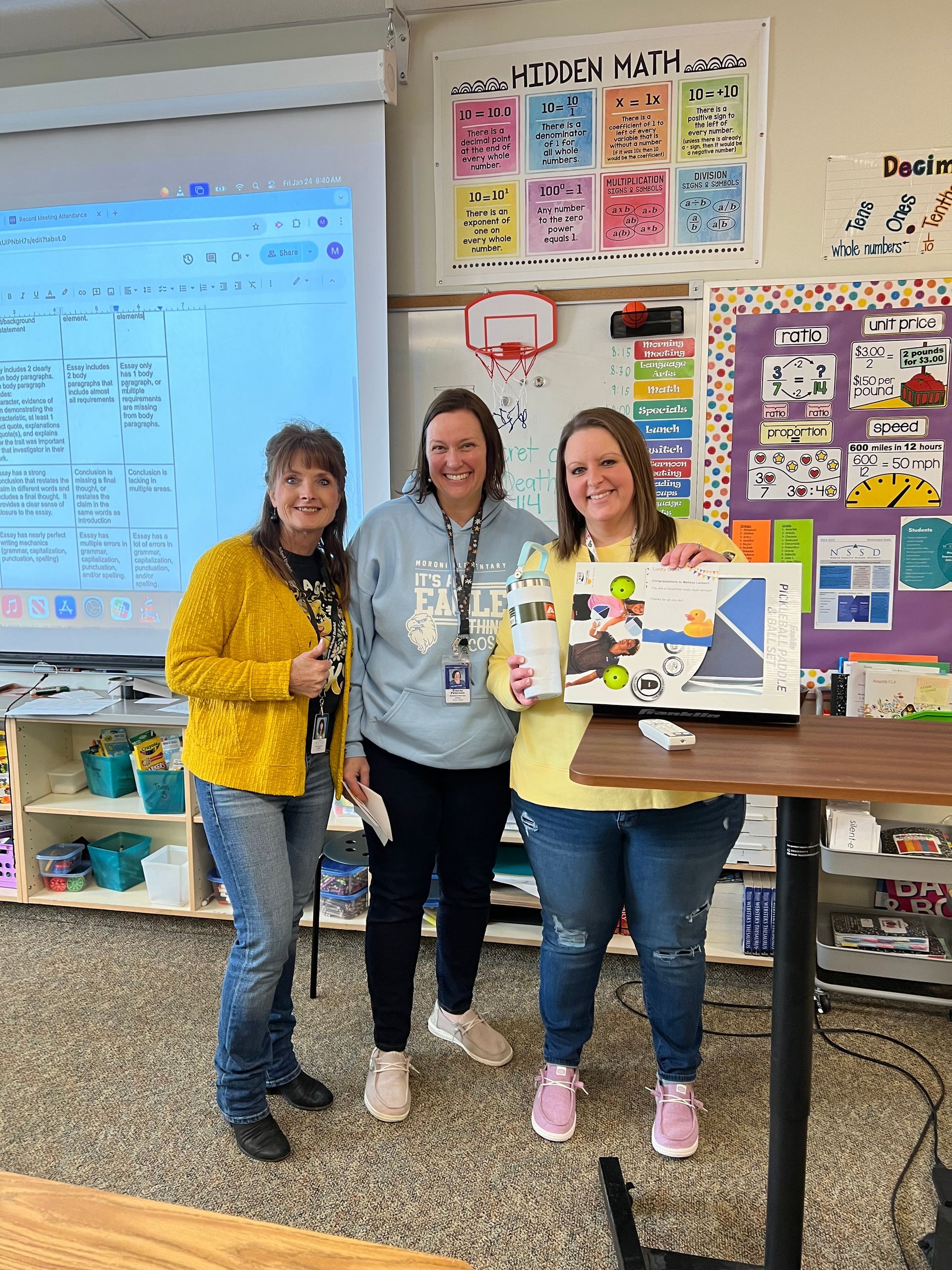 Three women are posing for a picture in a classroom.