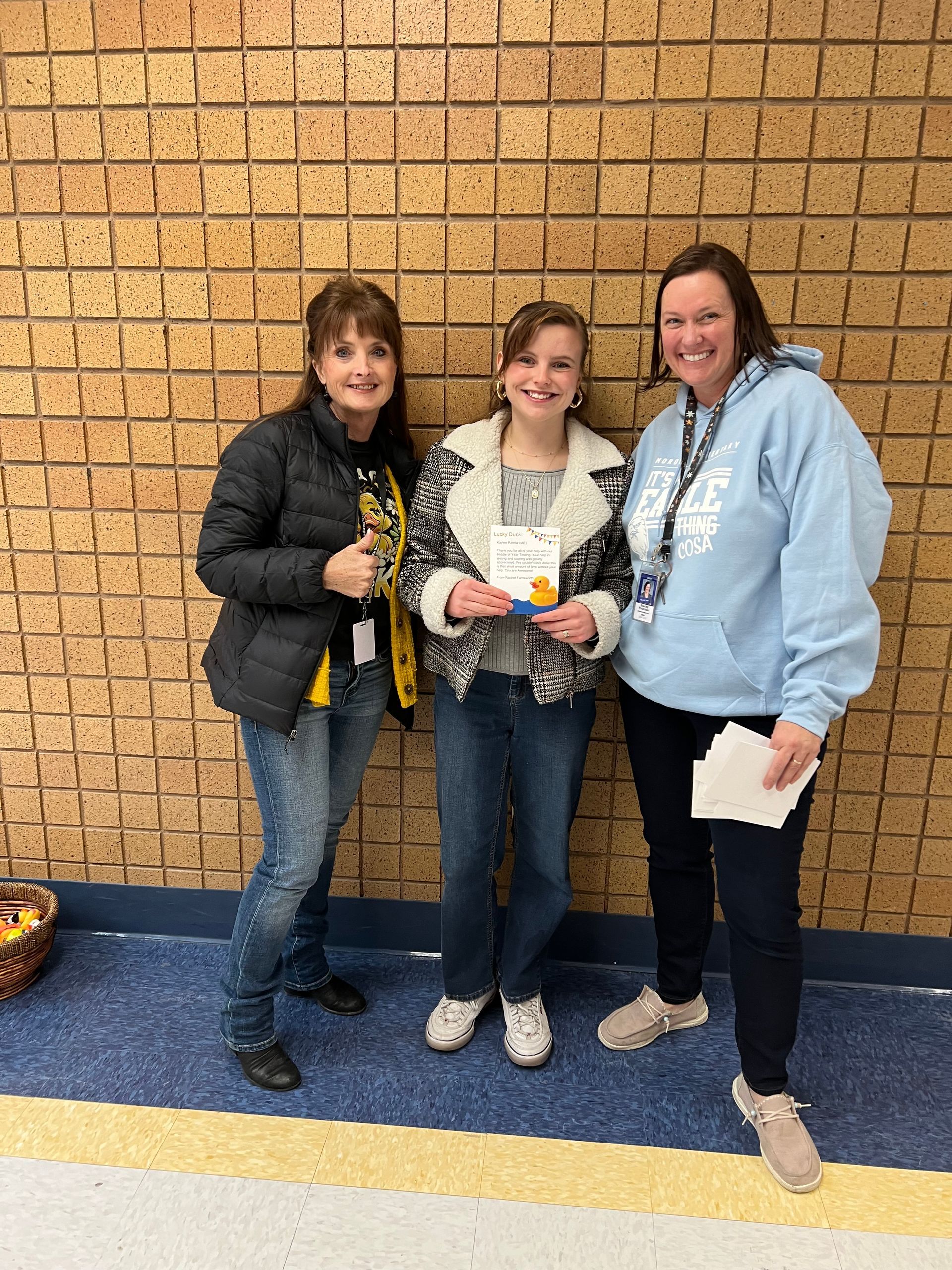 Three women are standing next to each other in front of a brick wall.