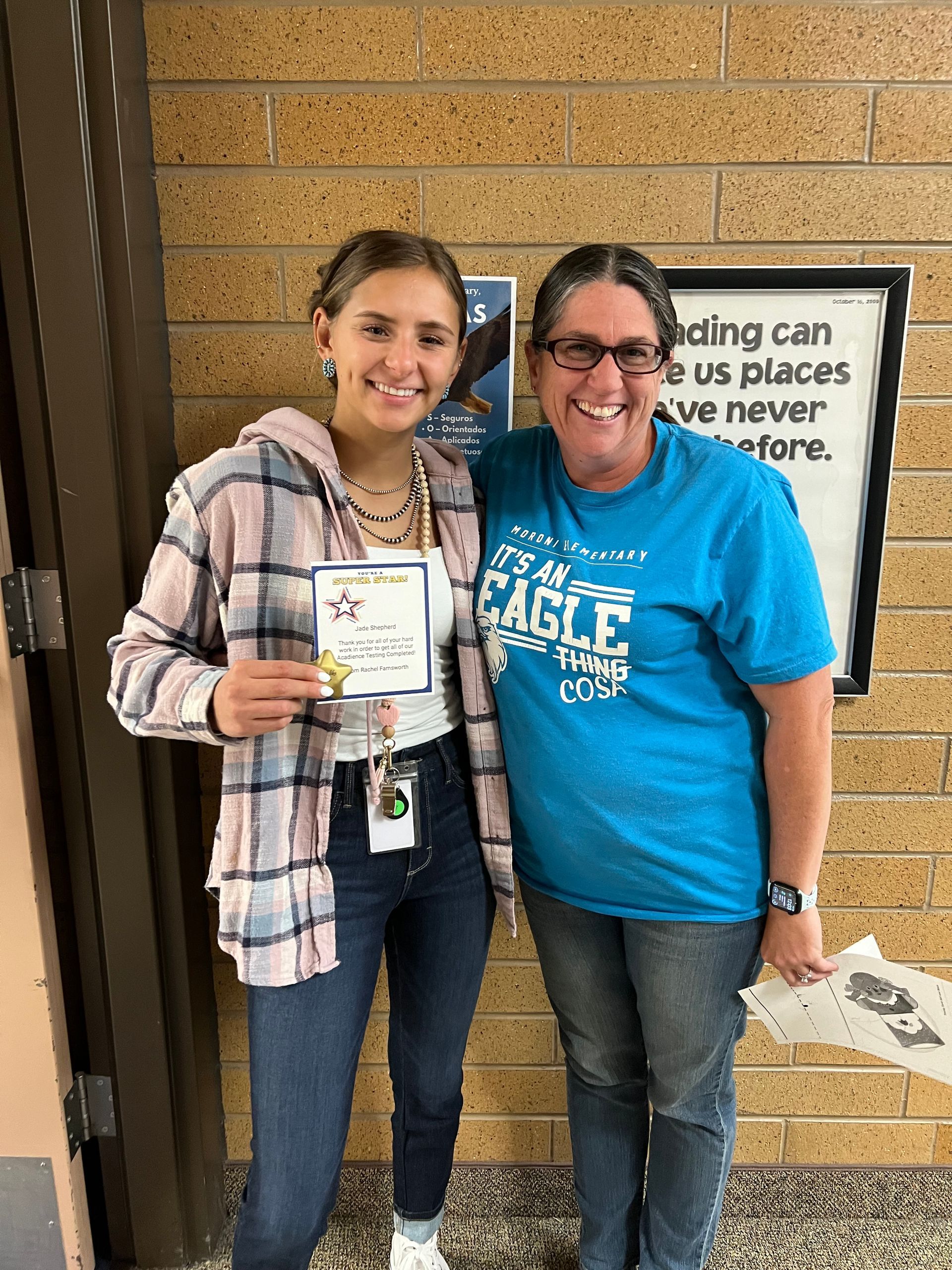 Woman in flannel holding award with woman in blue shirt in front of brick wall.