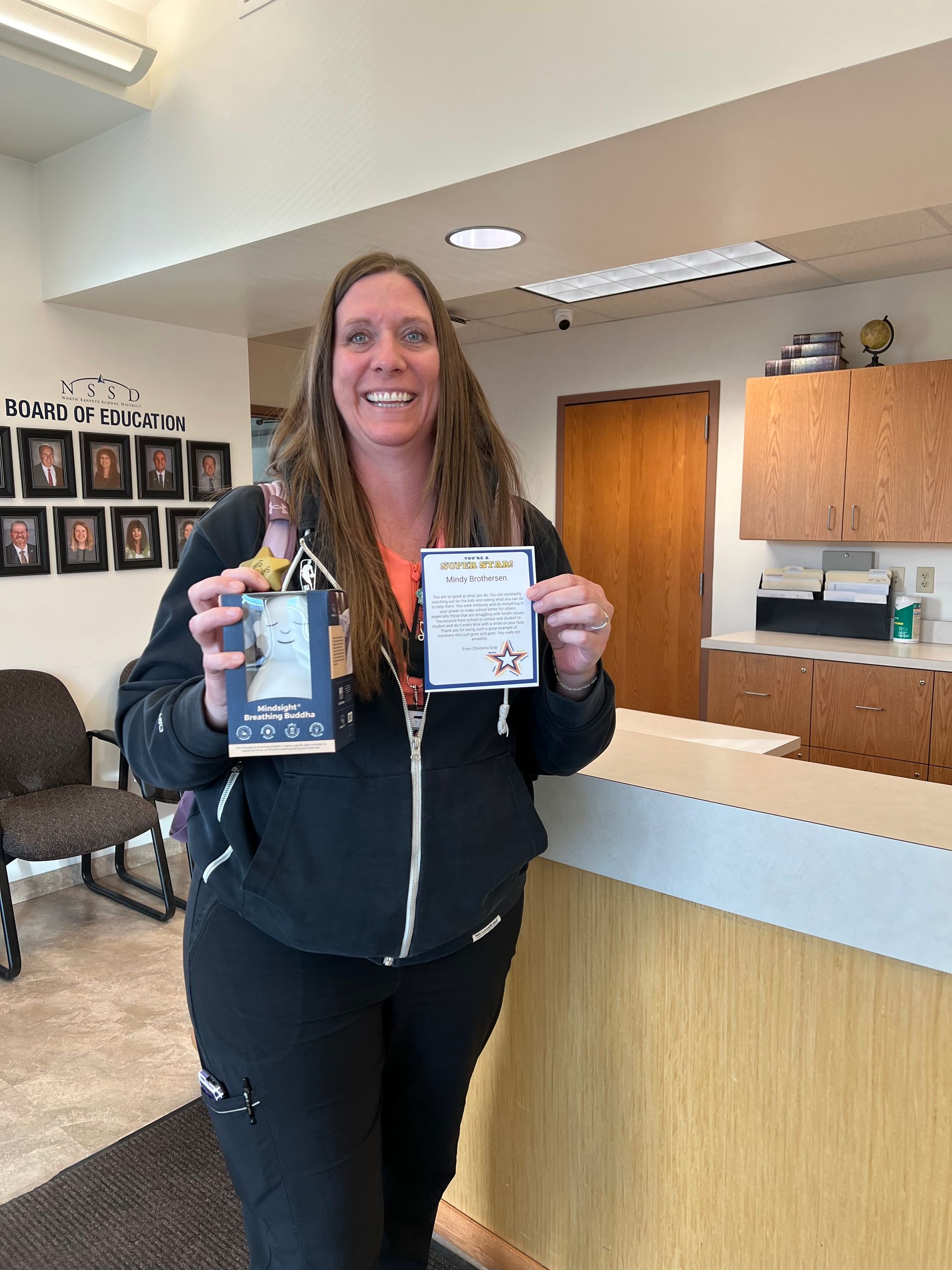 Woman in scrubs holding a gift and card smiling in an office setting.