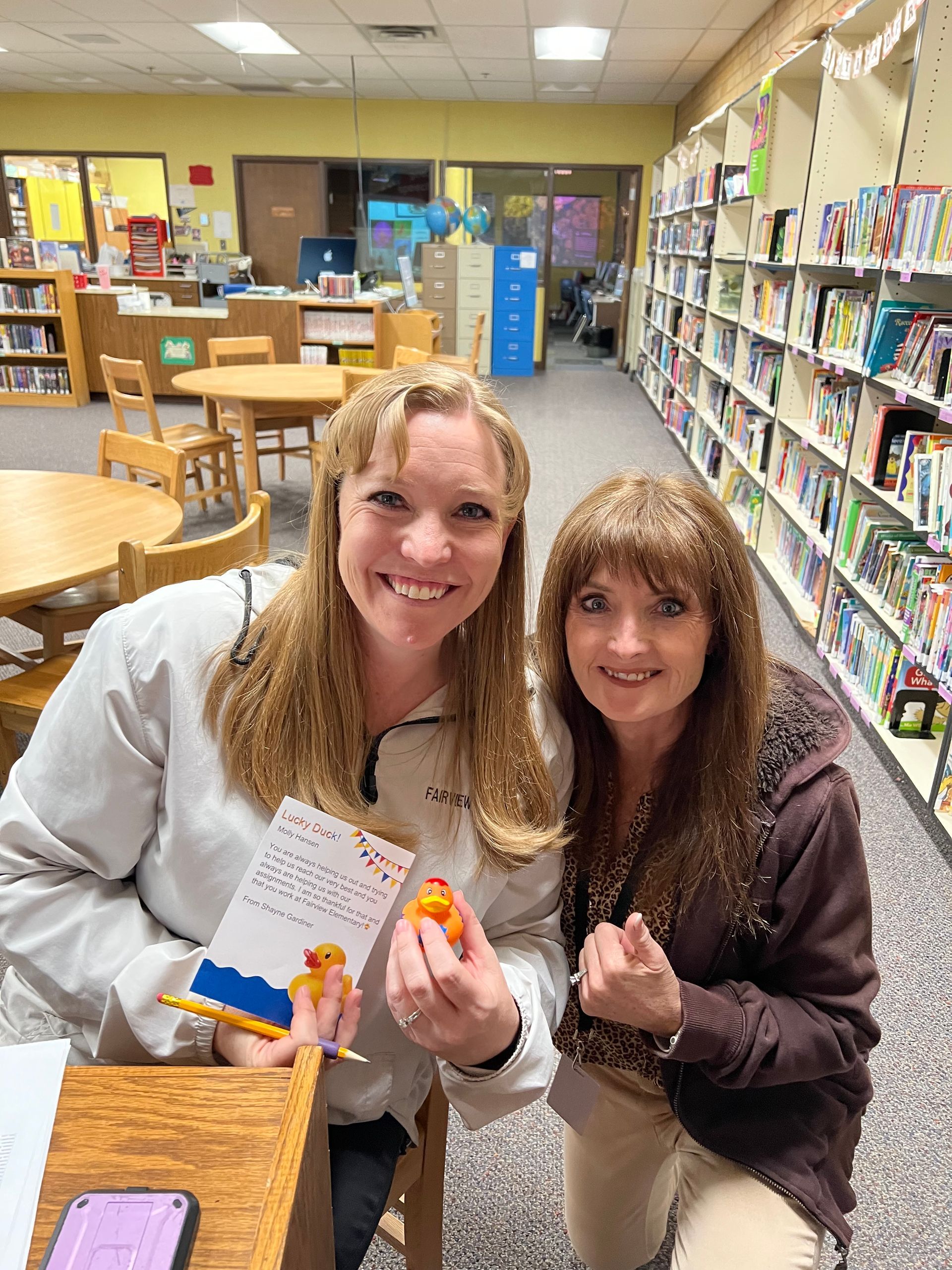 Two women are posing for a picture in a library.