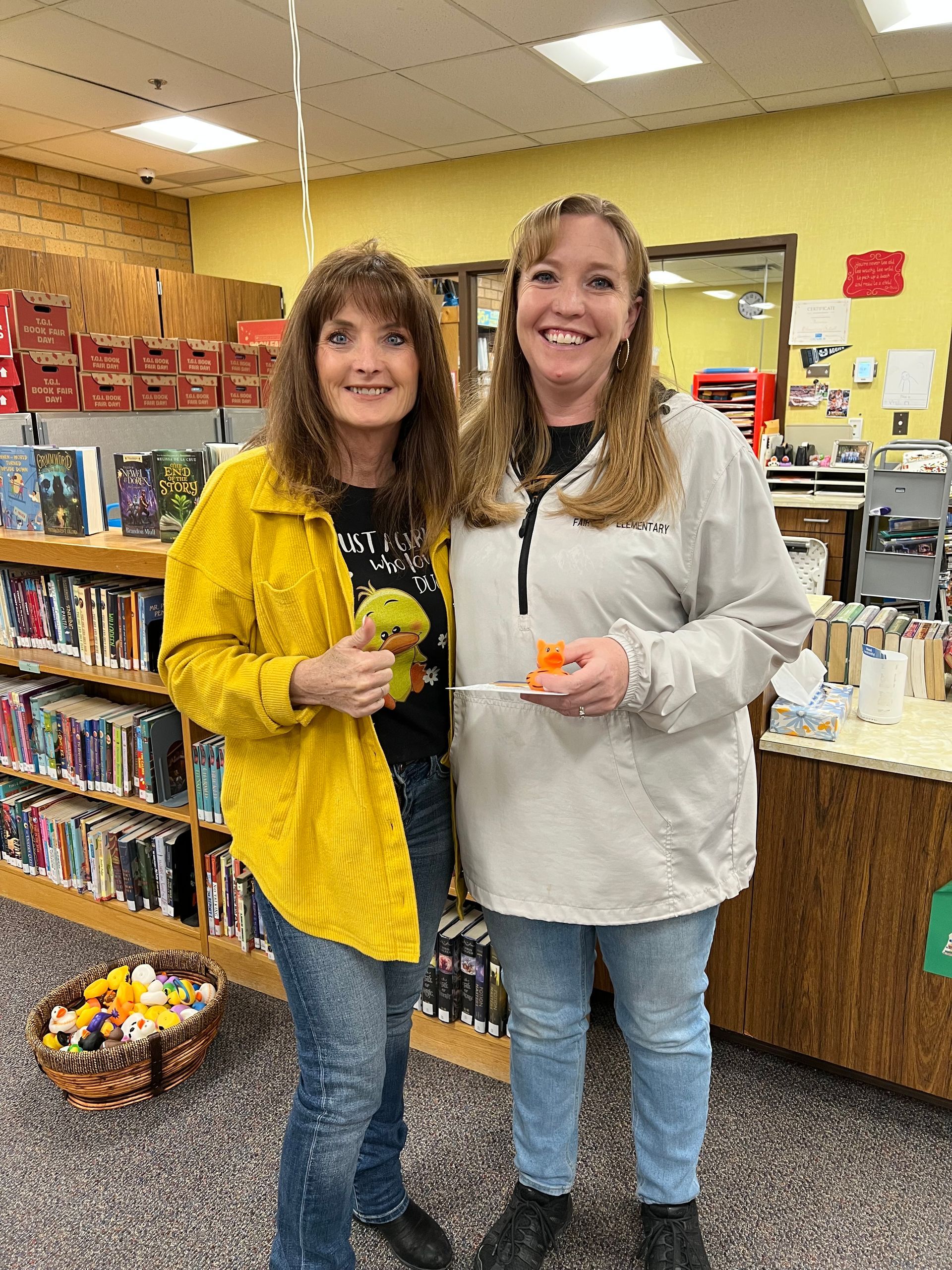 Two women are standing next to each other in a library holding a piece of cake.