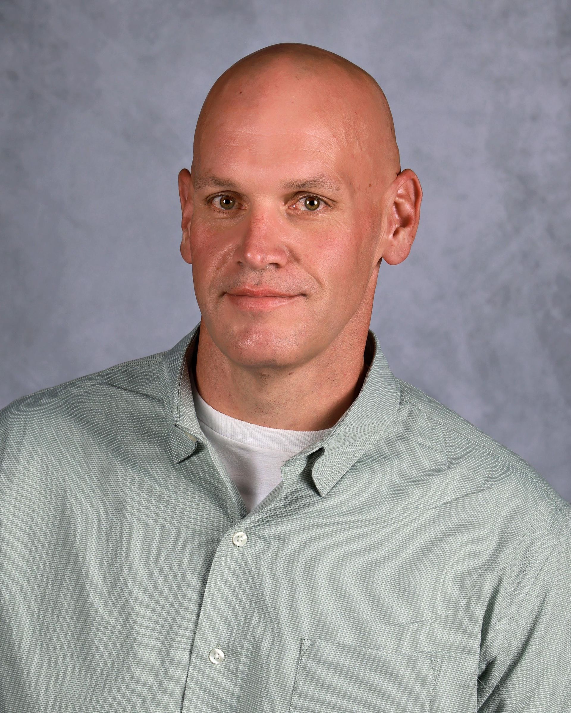 Bald man in a green and white striped shirt, smiling slightly, against a neutral background.