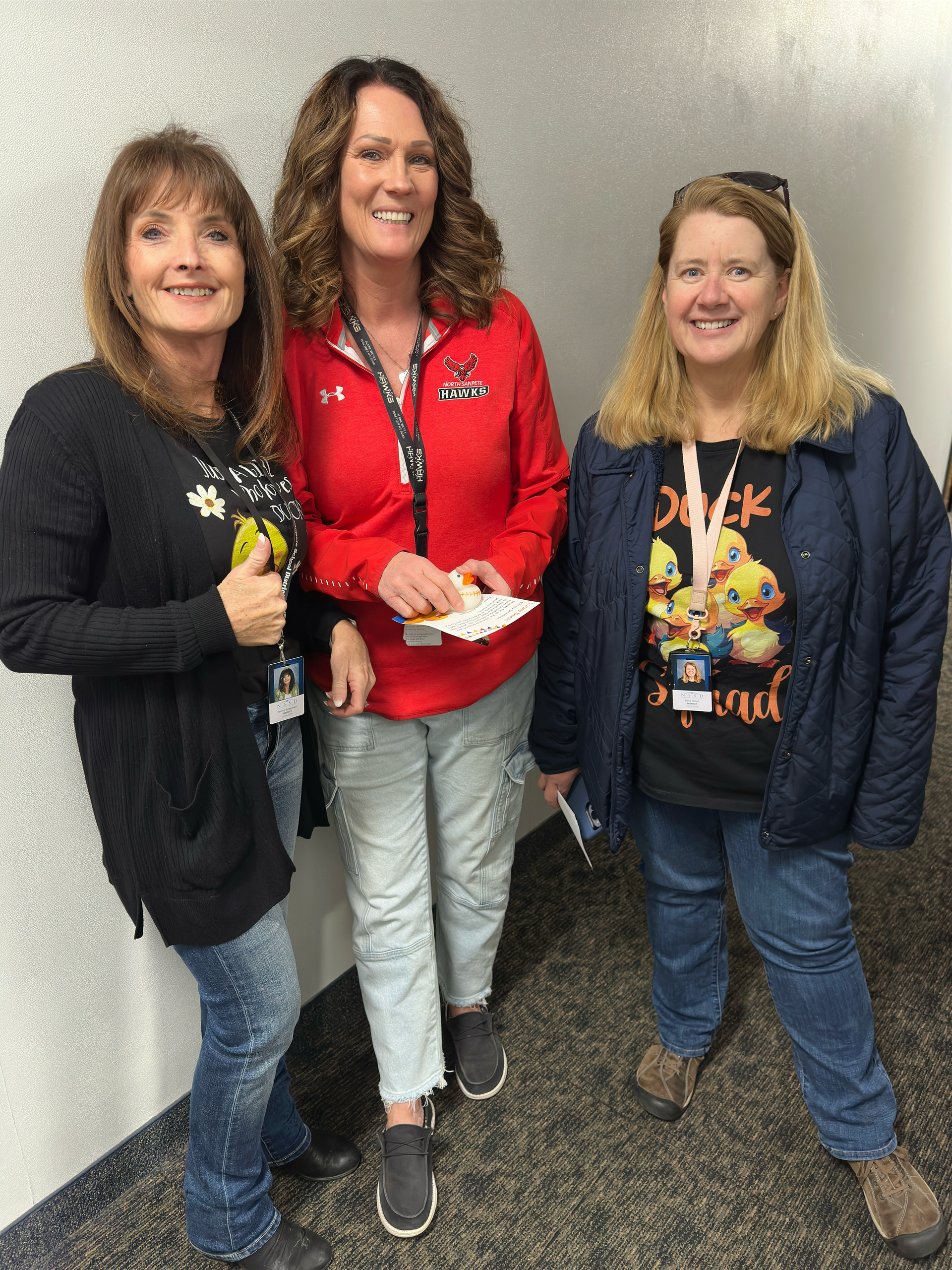 Three women are standing next to each other in a hallway.