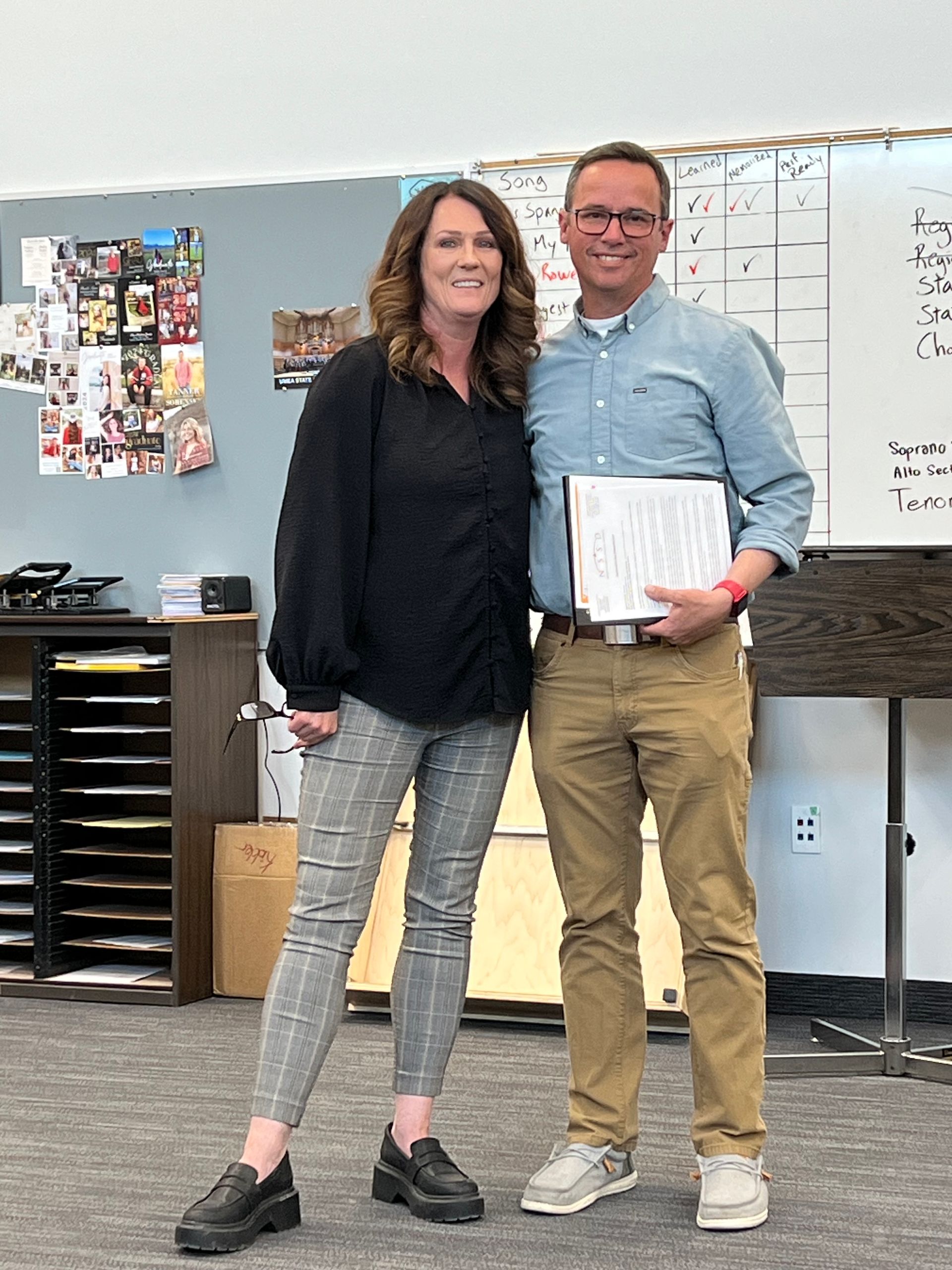 A man and a woman are standing next to each other in a classroom holding a certificate.
