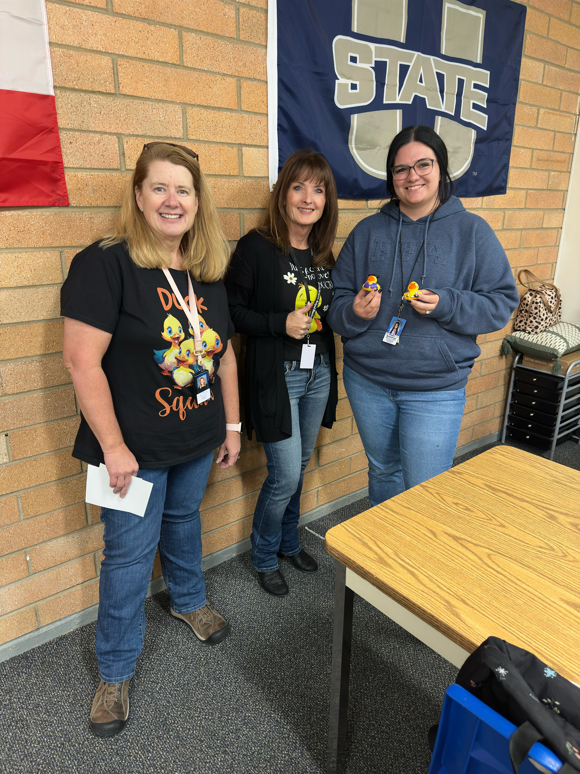 Three women are standing next to each other in front of a state flag.