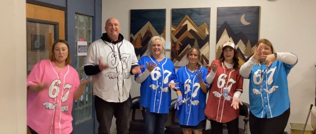 Group of people wearing baseball jerseys, gesturing with hands. Inside a building, art on wall.